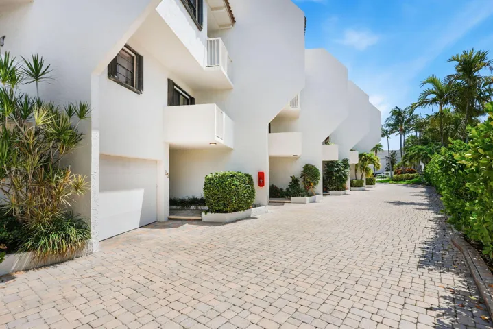 White stucco exterior with multiple balconies, private garages, and a paver driveway