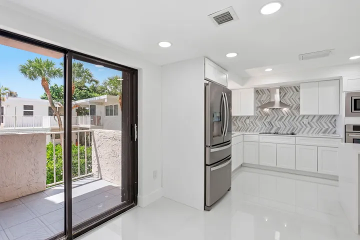 Modern kitchen featuring white cabinetry, stainless steel appliances, and a herringbone tile backsplash, dining area
