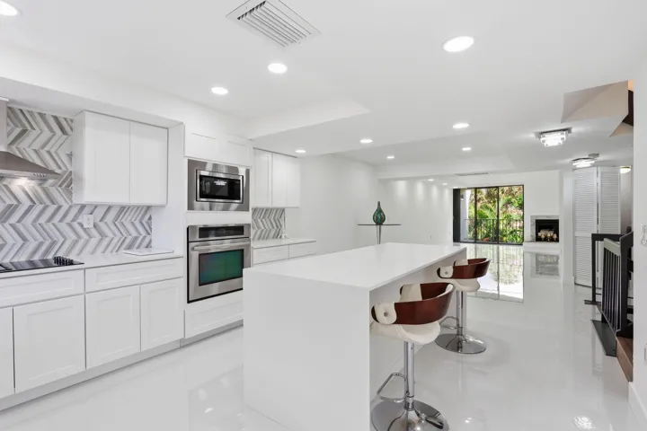 White shaker cabinetry, stainless steel appliances, herringbone tile backsplash, recessed lighting, and a kitchen island with a white countertop