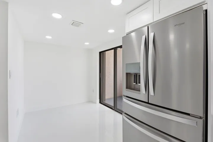 Stainless steel French door refrigerator, white cabinetry, recessed lighting, white flooring, and sliding glass door
