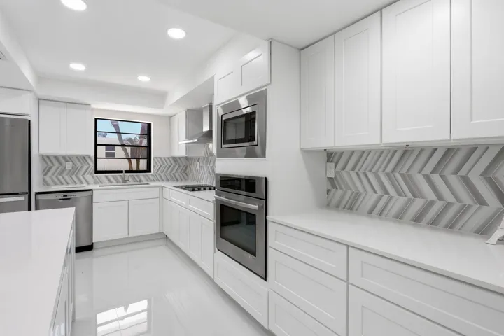 White cabinetry, stainless steel appliances, herringbone-patterned backsplash, recessed lighting, and a window above the sink