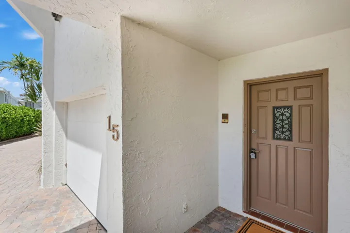 Textured exterior wall finish, paneled entry door with decorative ironwork, integrated garage door, and a brick paver driveway