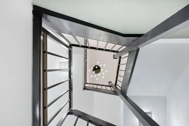 Architectural staircase with metal railings, white walls, and a multi-bulb ceiling fixture