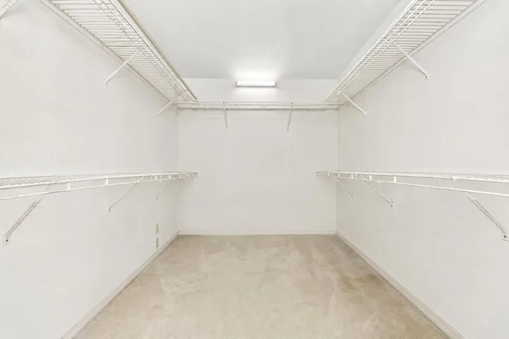 Generous walk-in closet with white wire shelving, hanging rods, and neutral-toned carpeting