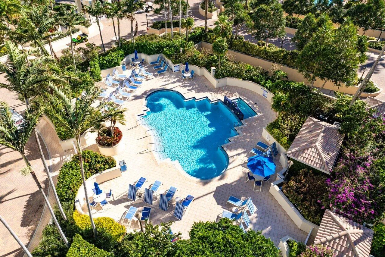 Resort-style pool area with a freeform swimming pool, integrated spa, paver decking, lush landscaping, and cabana structure