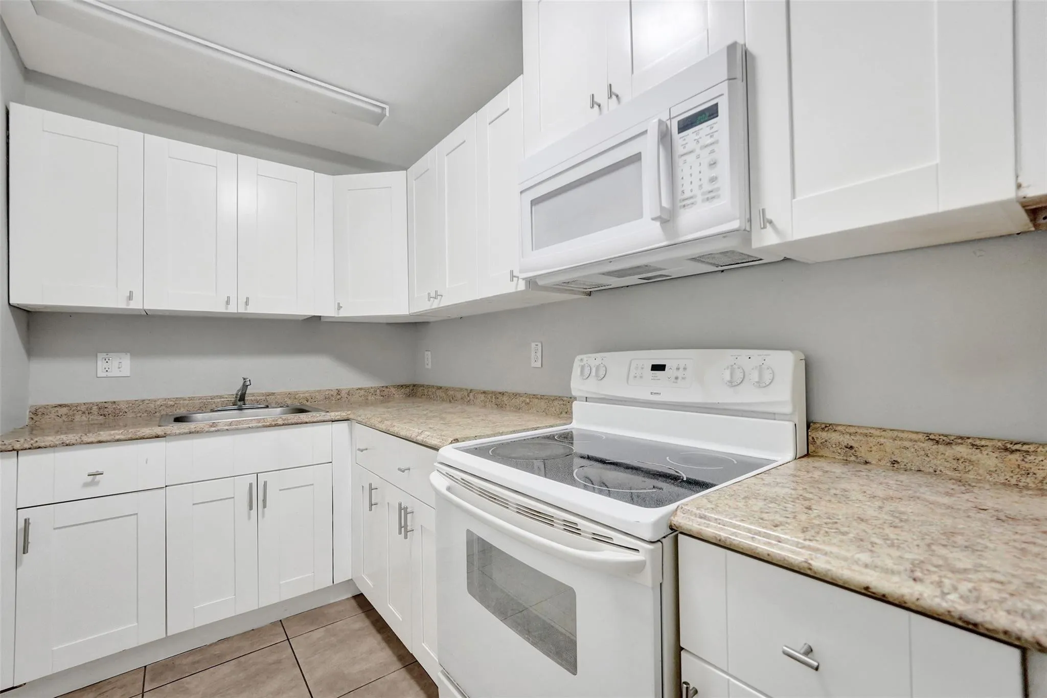 Bright, updated kitchen featuring white cabinetry with brushed nickel hardware, granite-style countertops, tile flooring, and stainless steel appliances including a slide-in electric range, microwave, and dishwasher