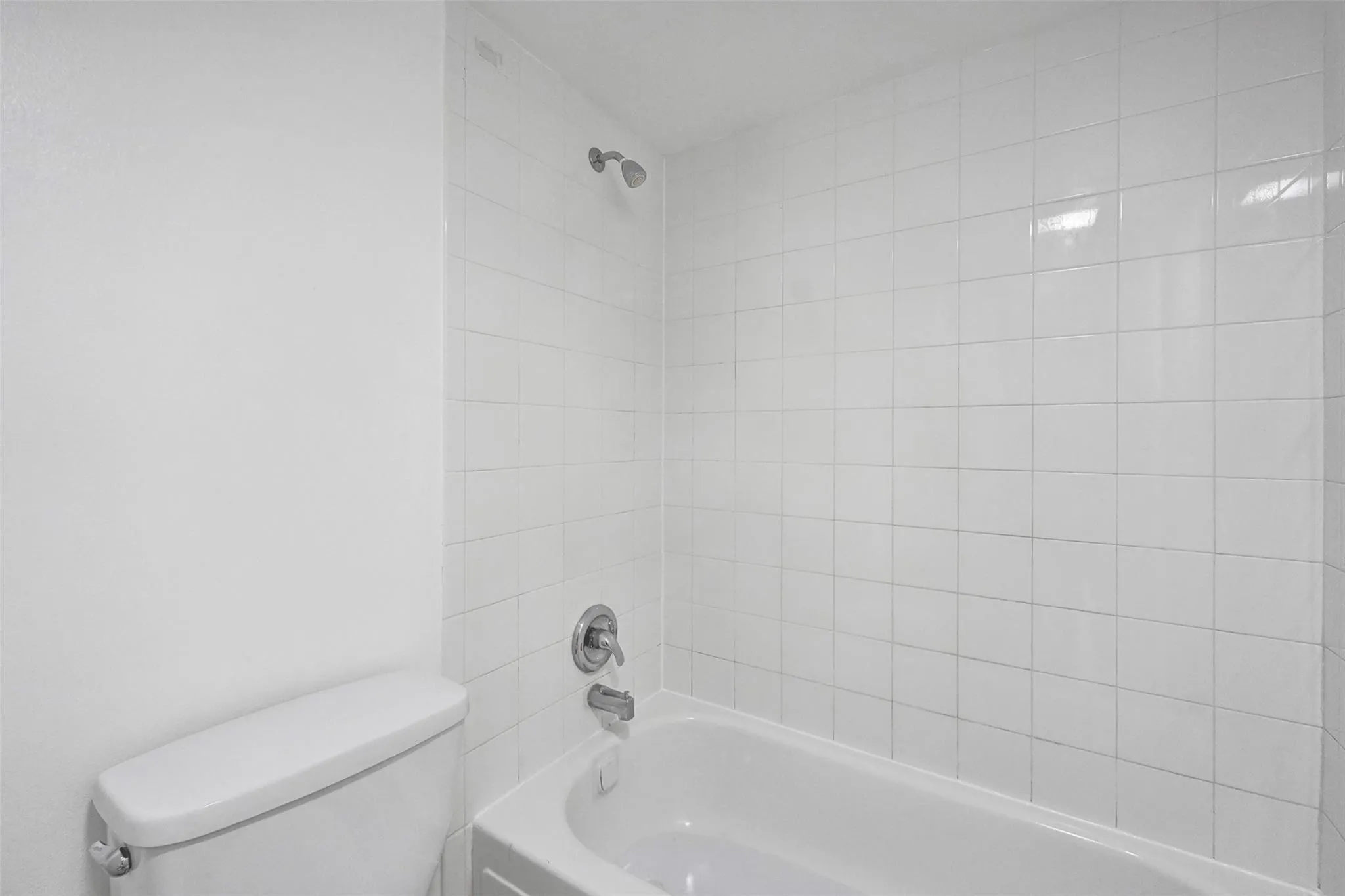 Clean bathroom featuring white subway tile surround, white porcelain bathtub with chrome fixtures, and chrome showerhead with valve controls