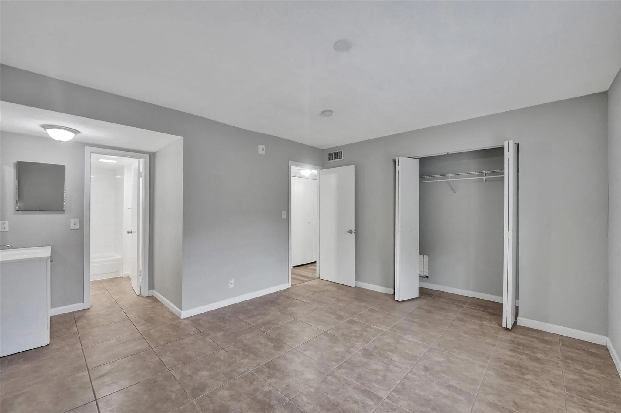 Spacious primary suite featuring wood-finish flooring, multiple closet systems with sliding glass doors, recessed ceiling lighting, and an ensuite bathroom with vanity and tile flooring