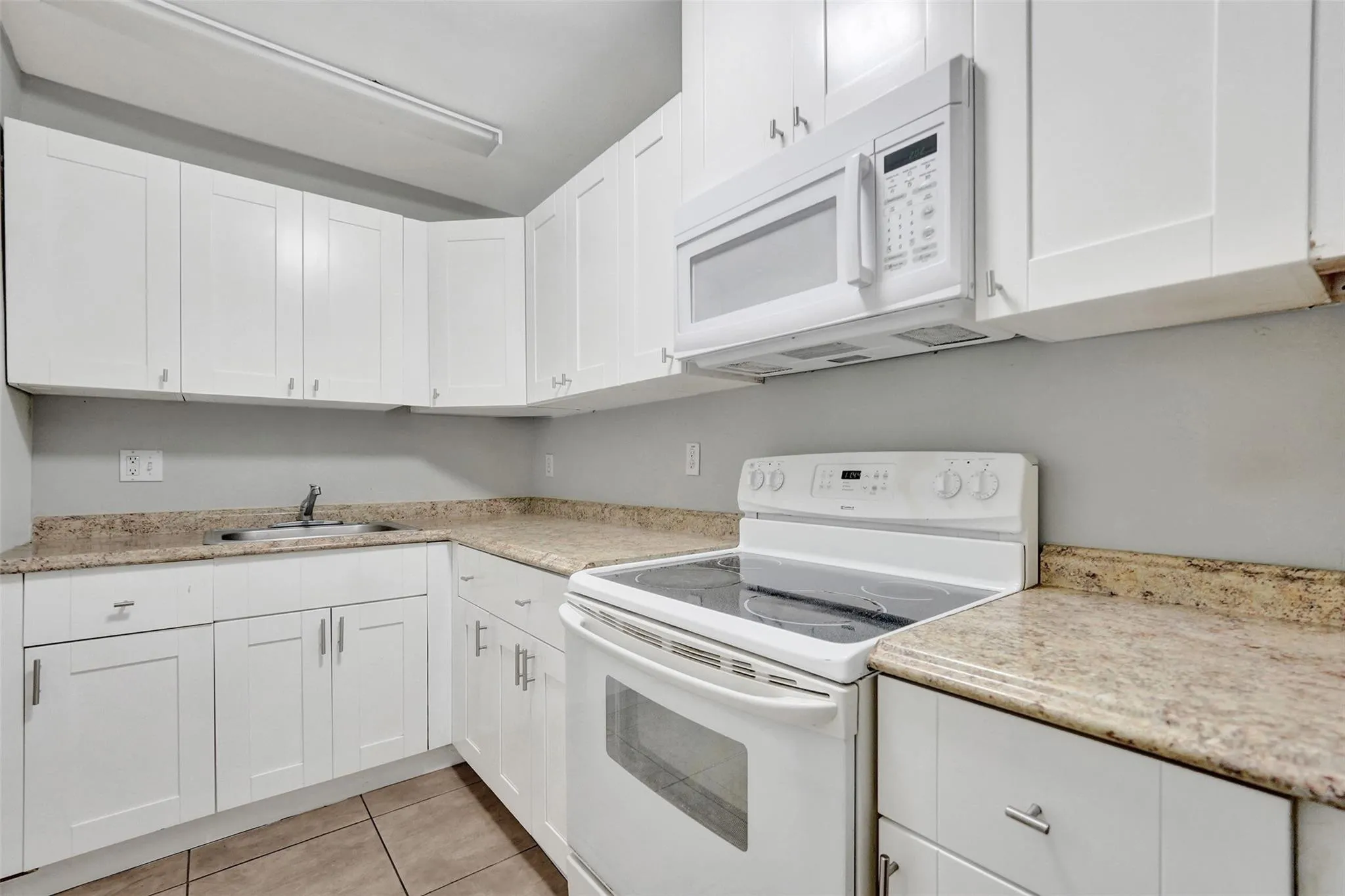 White cabinetry, integrated microwave, built-in electric range, stainless steel sink, and tile flooring