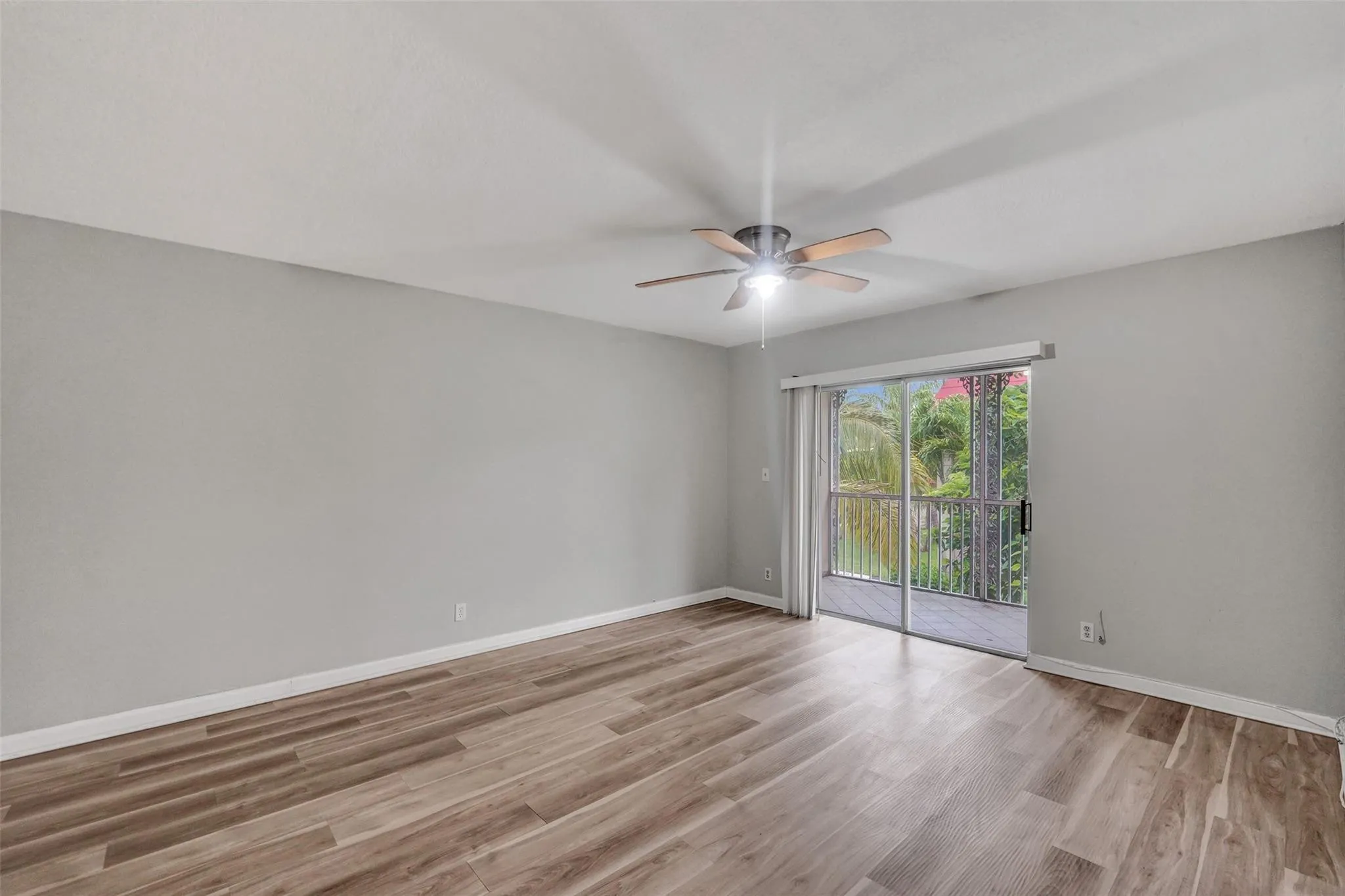 Bright, open room showcasing warm wood-finish flooring, neutral gray walls, and ceiling fan with integrated lighting