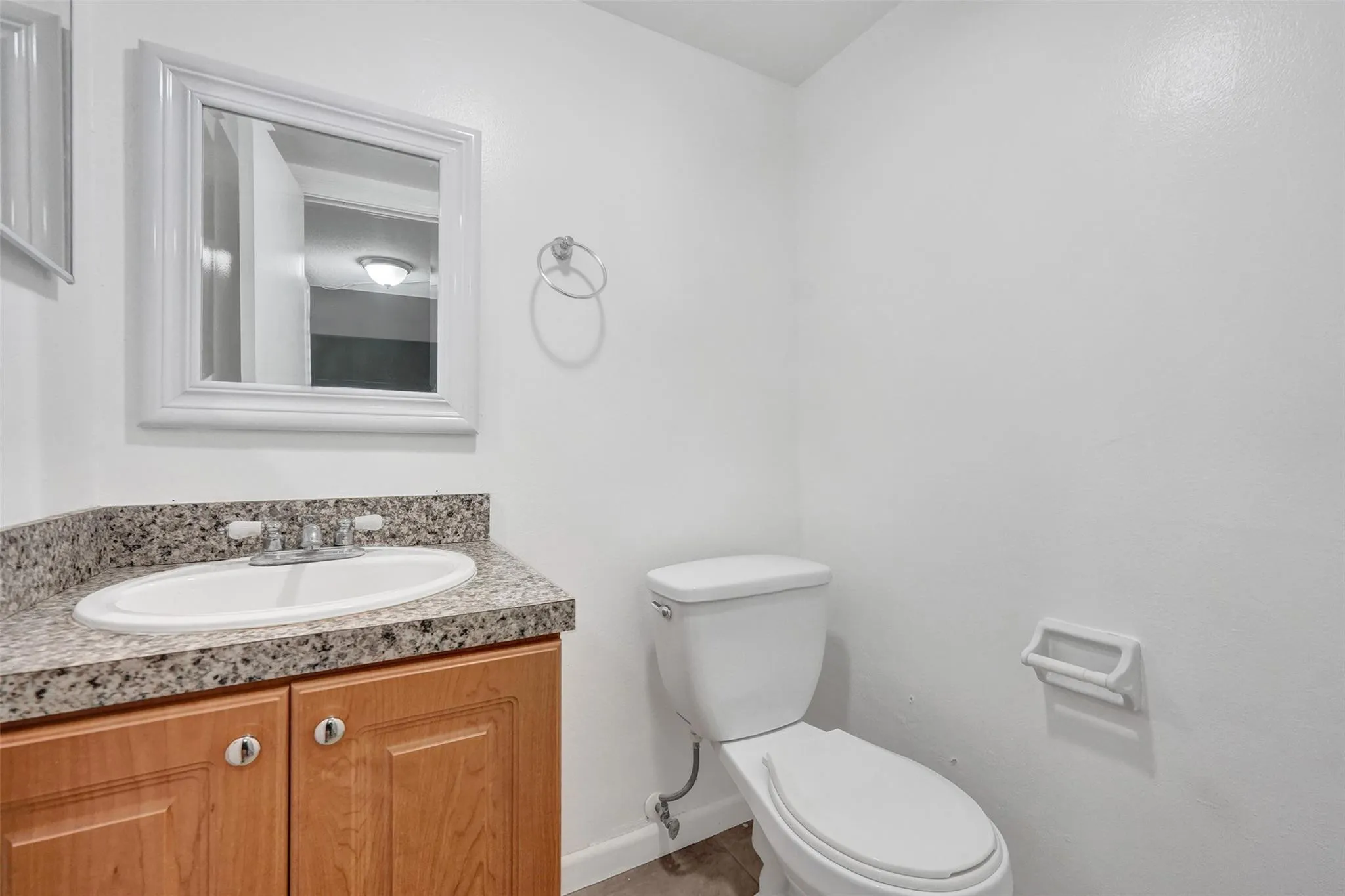 Bright and functional bathroom featuring a wood-finish vanity with dual handles, speckled stone countertop, and chrome fixtures
