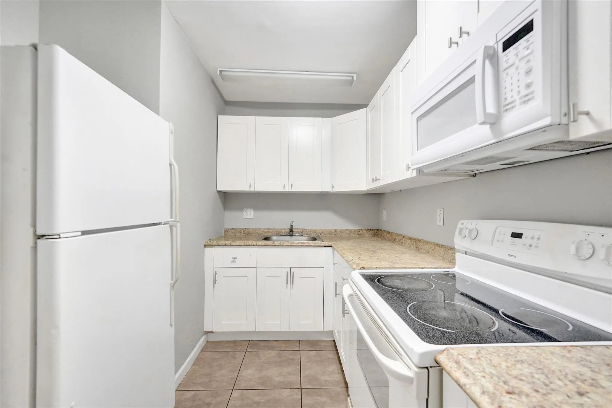 White cabinetry with brushed nickel hardware, laminate countertops, tile flooring, built-in microwave, and electric range