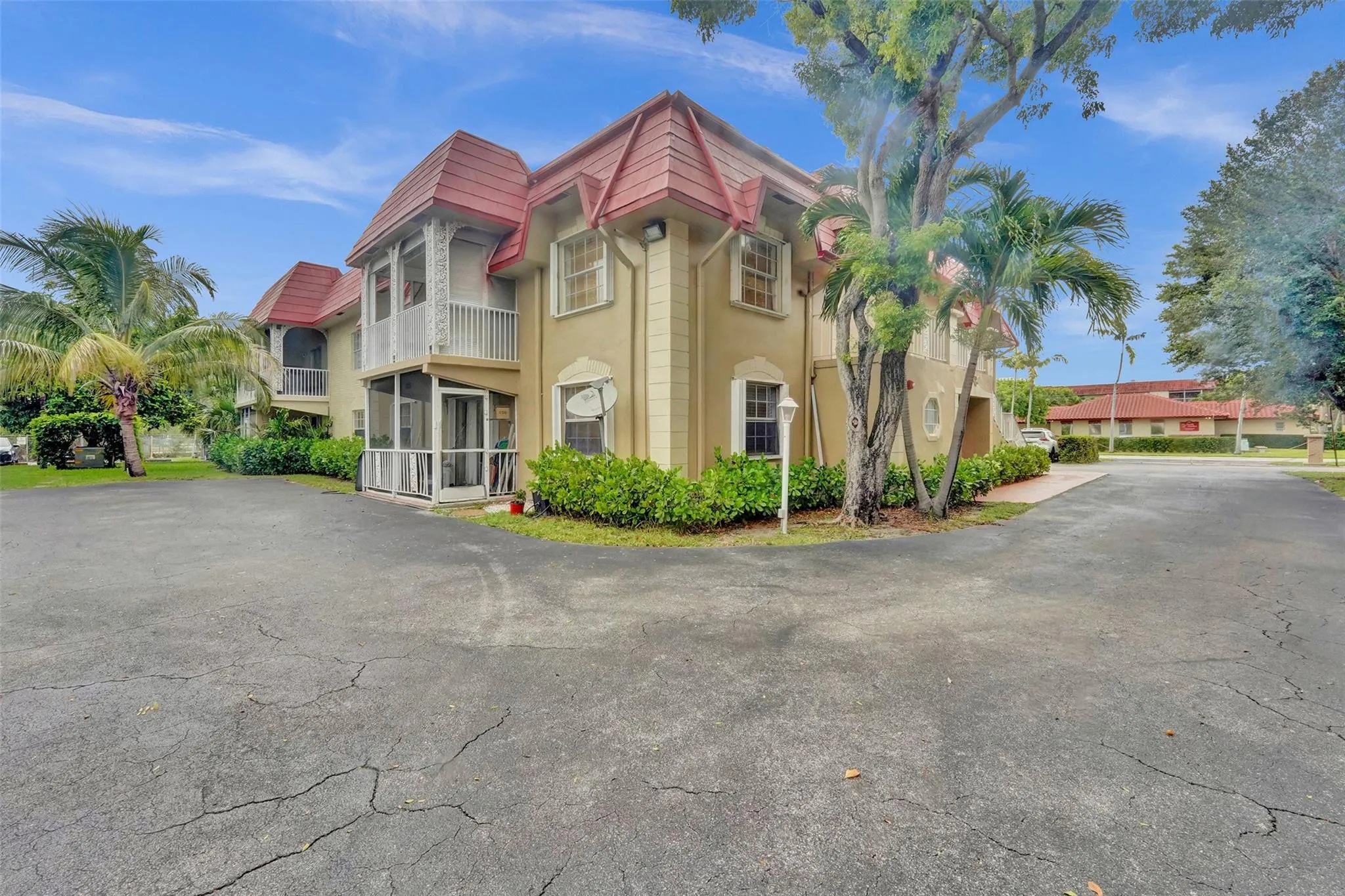 Distinctive French Colonial estate featuring a cream-finish exterior with burgundy metal roof accents, arched architectural detailing, and multi-pane windows