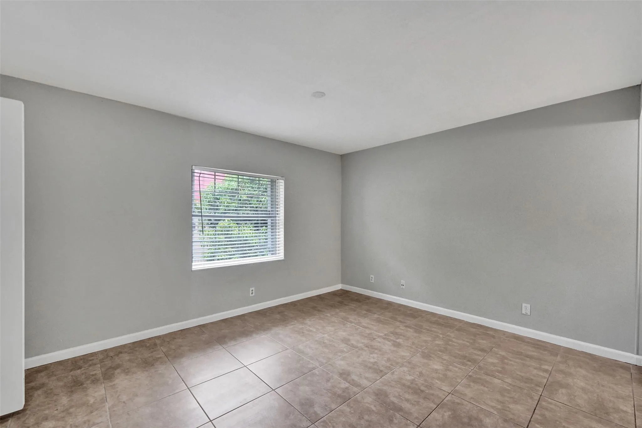 Neutral gray wall color, tiled flooring, window with horizontal blinds, and white trim accents