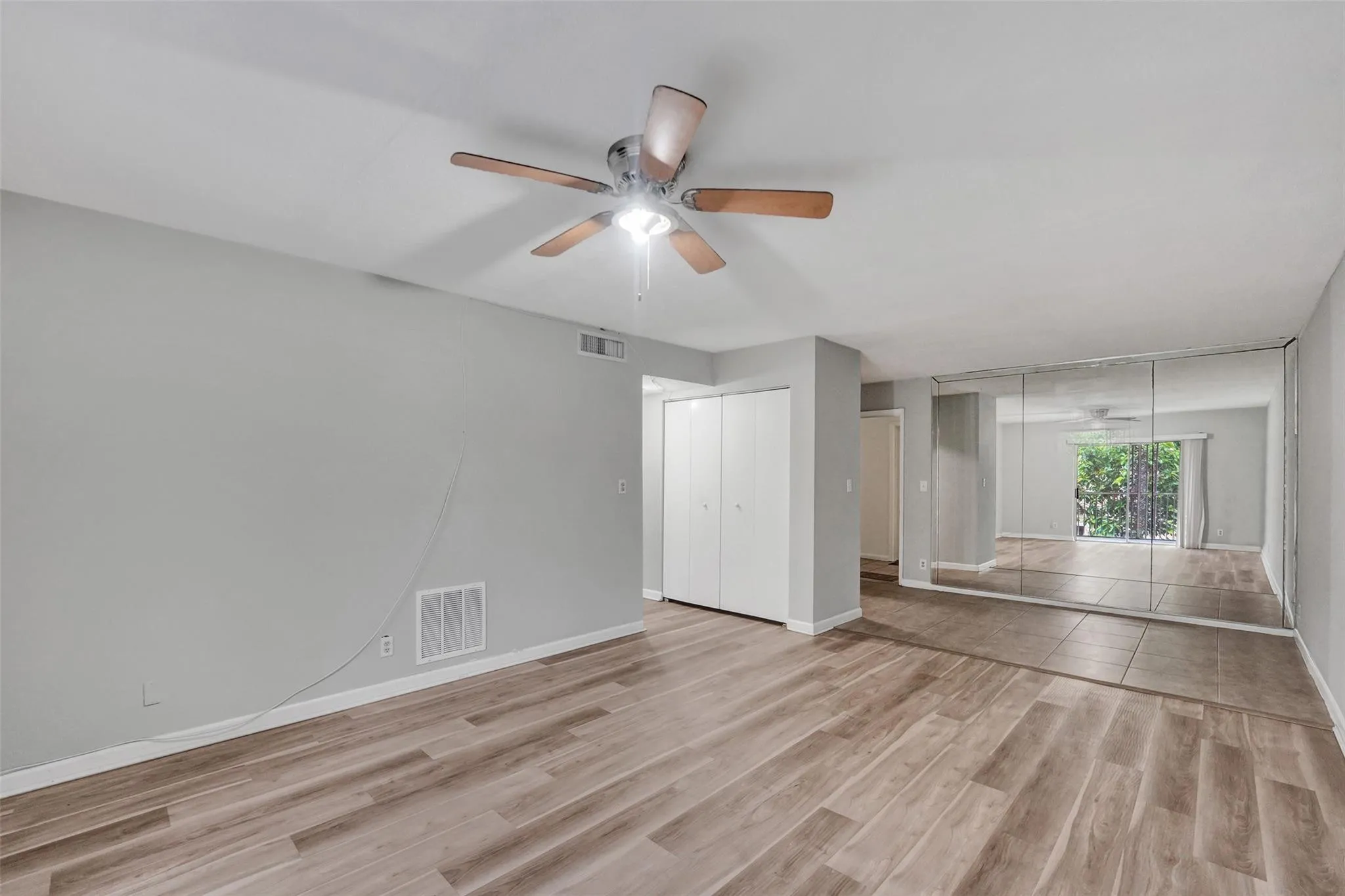 Spacious primary bedroom featuring wood-finish flooring throughout, a ceiling fan with integrated lighting, and mirrored closet doors