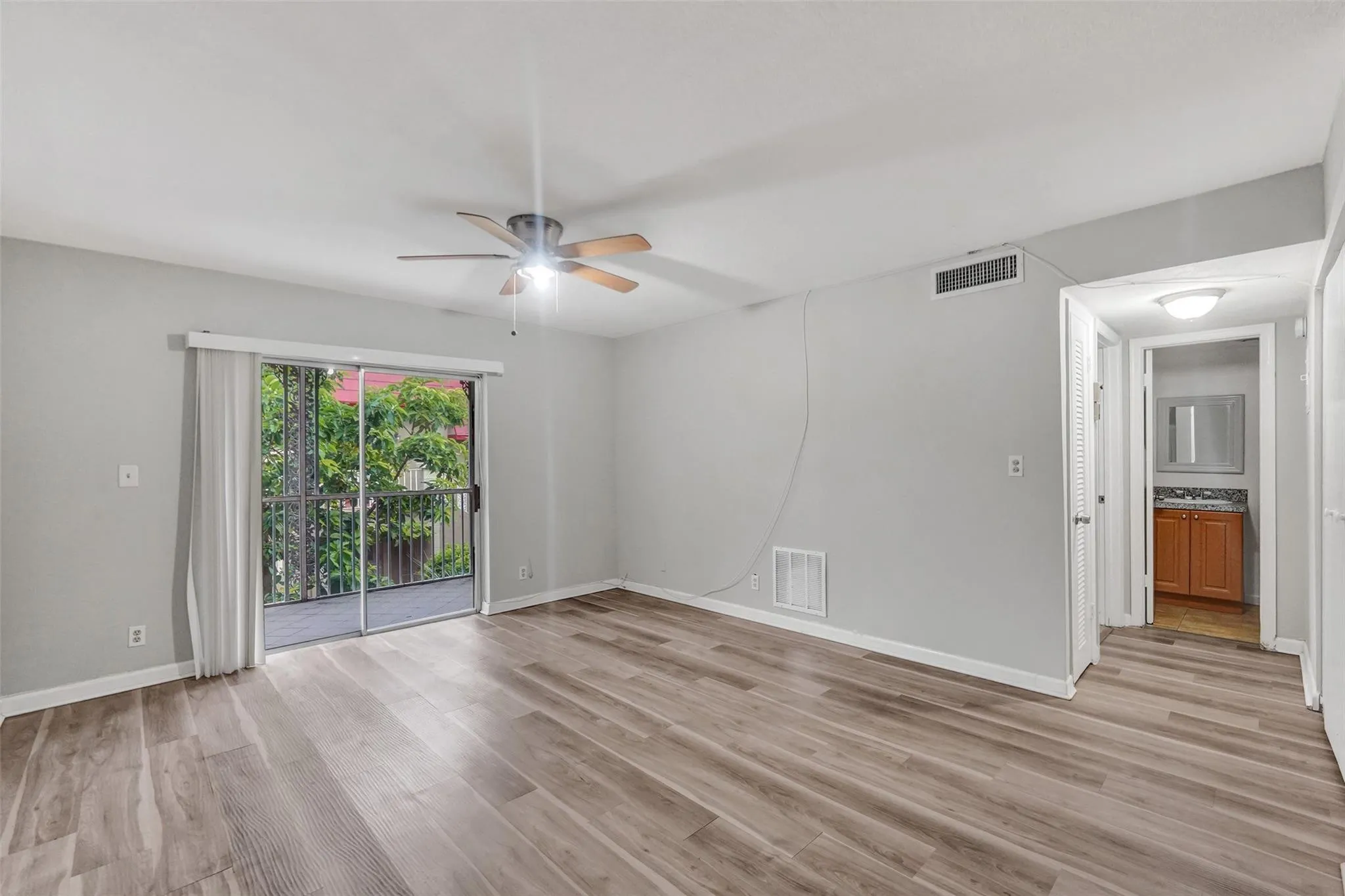 Spacious living area with wood-finish flooring, ceiling fan with integrated lighting, and sliding glass doors opening to outdoor space