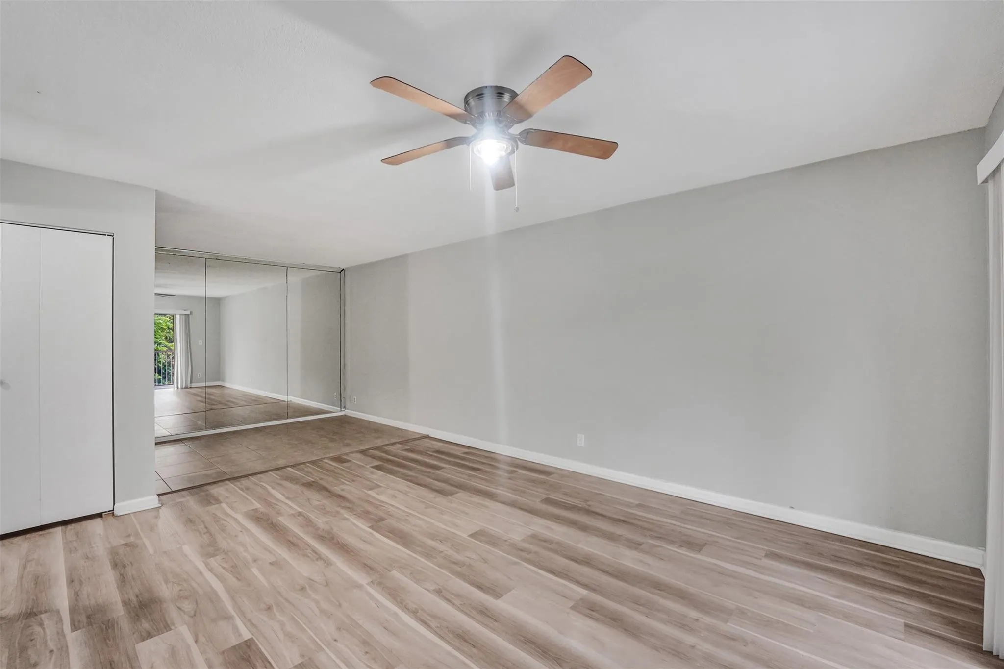 Wood-finish flooring, ceiling fan, mirrored wall, and solid panel closet doors