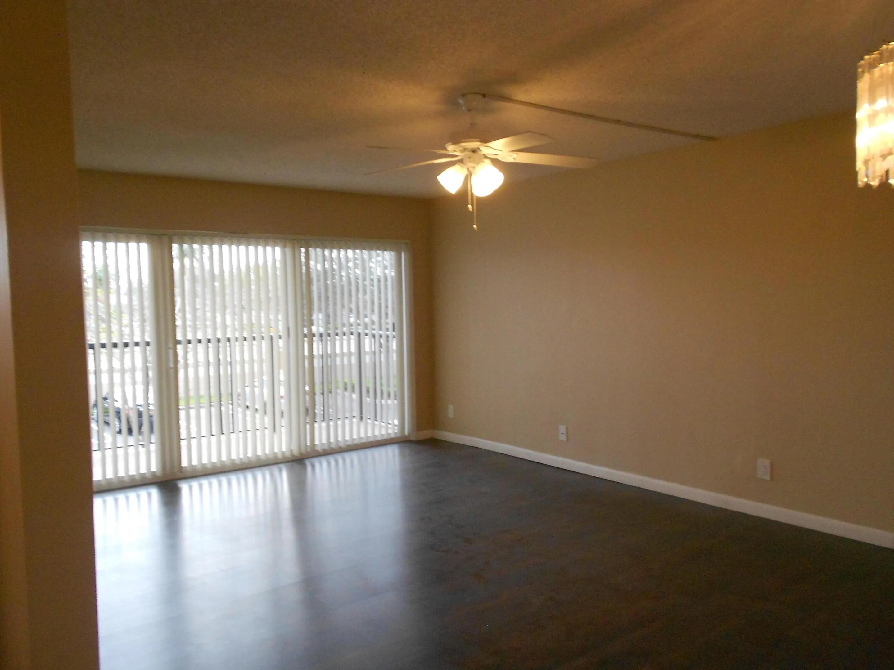 Spacious living area featuring gleaming wood-finish flooring, neutral wall finishes, and abundant natural light from expansive glass sliding doors