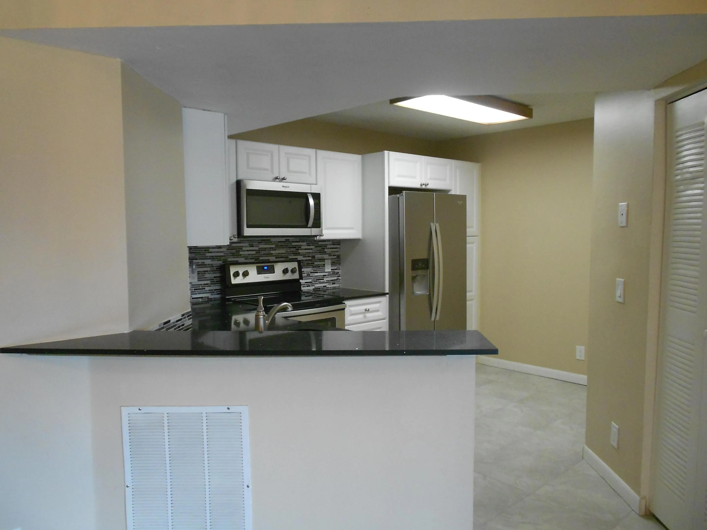 Modern kitchen featuring stainless steel appliances, including a gas cooktop and refrigerator with ice and water dispensers, dark countertops, white cabinetry, and a tile backsplash