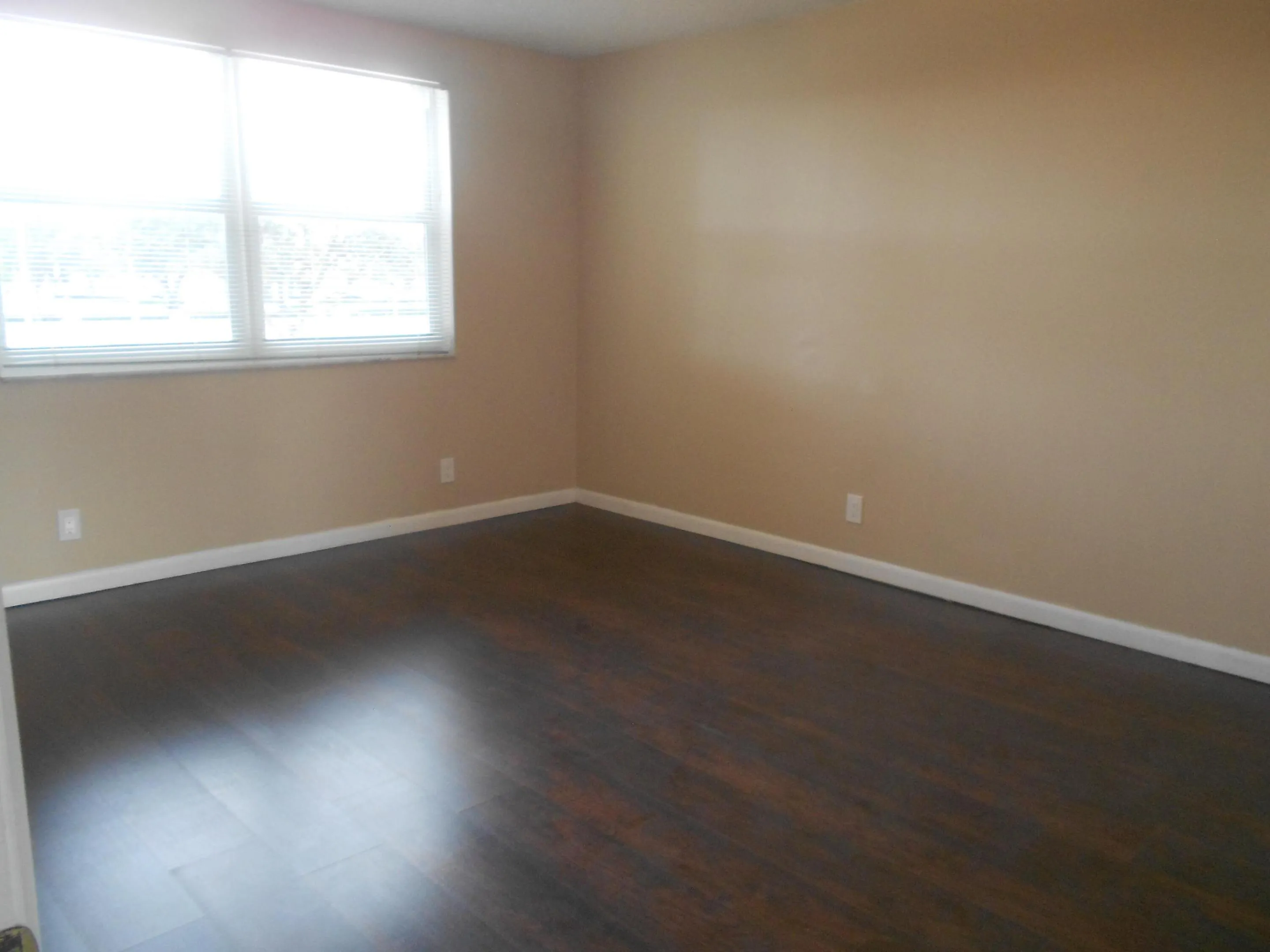 Spacious room showcasing rich wood-finish flooring, neutral wall tones, and abundant natural light from a large window