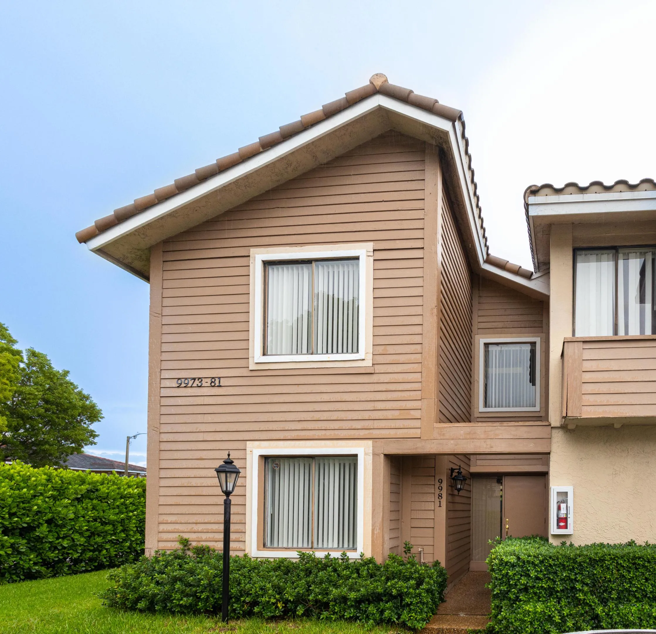 Stucco exterior with horizontal siding, tile roof, and manicured shrubbery
