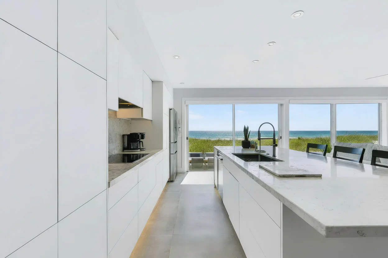 White flat-panel cabinetry, a large kitchen island with a stone countertop, a built-in cooktop, and floor-to-ceiling windows