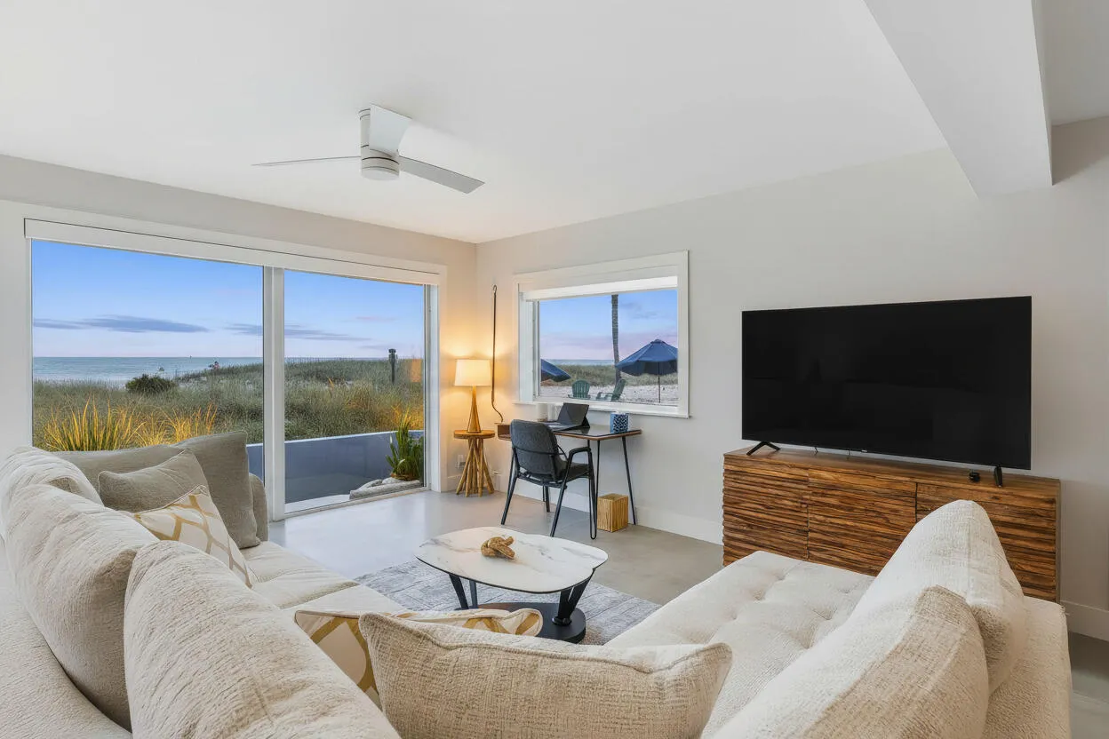 Expansive sliding glass doors, white window trim, wood-finish media console, and a ceiling fan