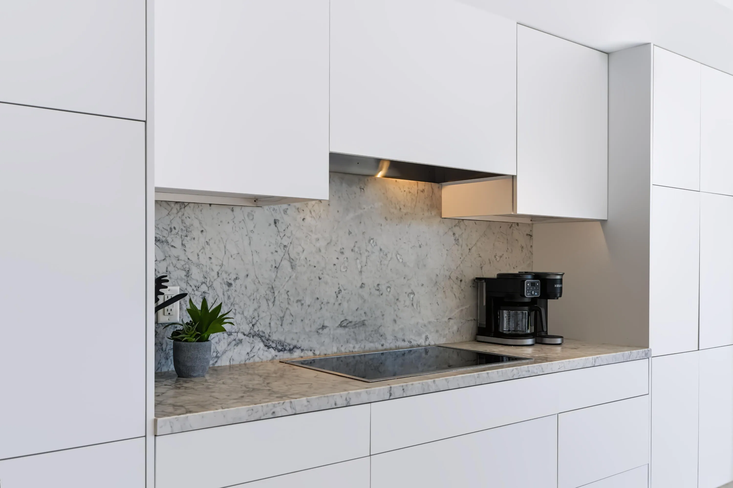Integrated cooktop with light-toned countertop, white cabinetry, and stone backsplash