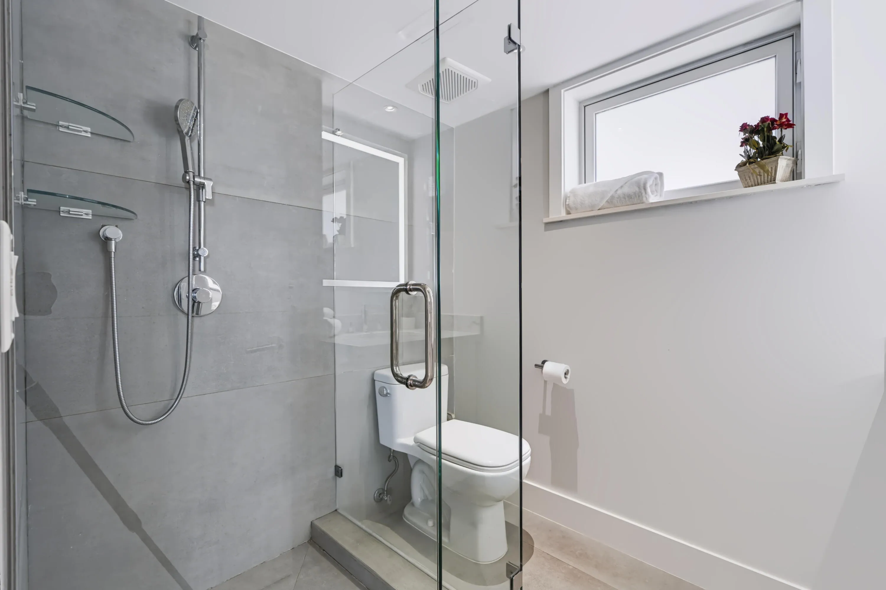 Glass-enclosed shower with gray tiled walls, chrome fixtures, and a toilet