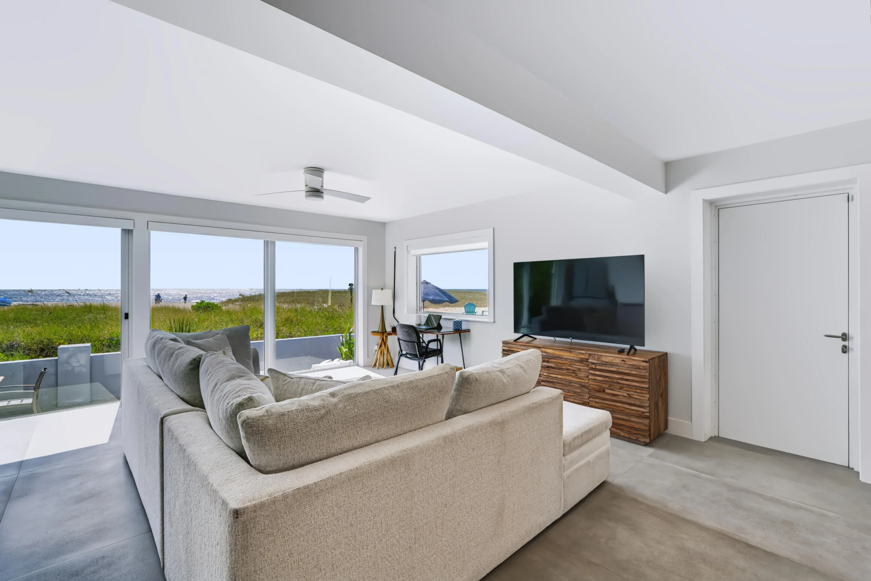Expansive sliding glass doors, concrete flooring, a contemporary ceiling fan, and a built-in media console