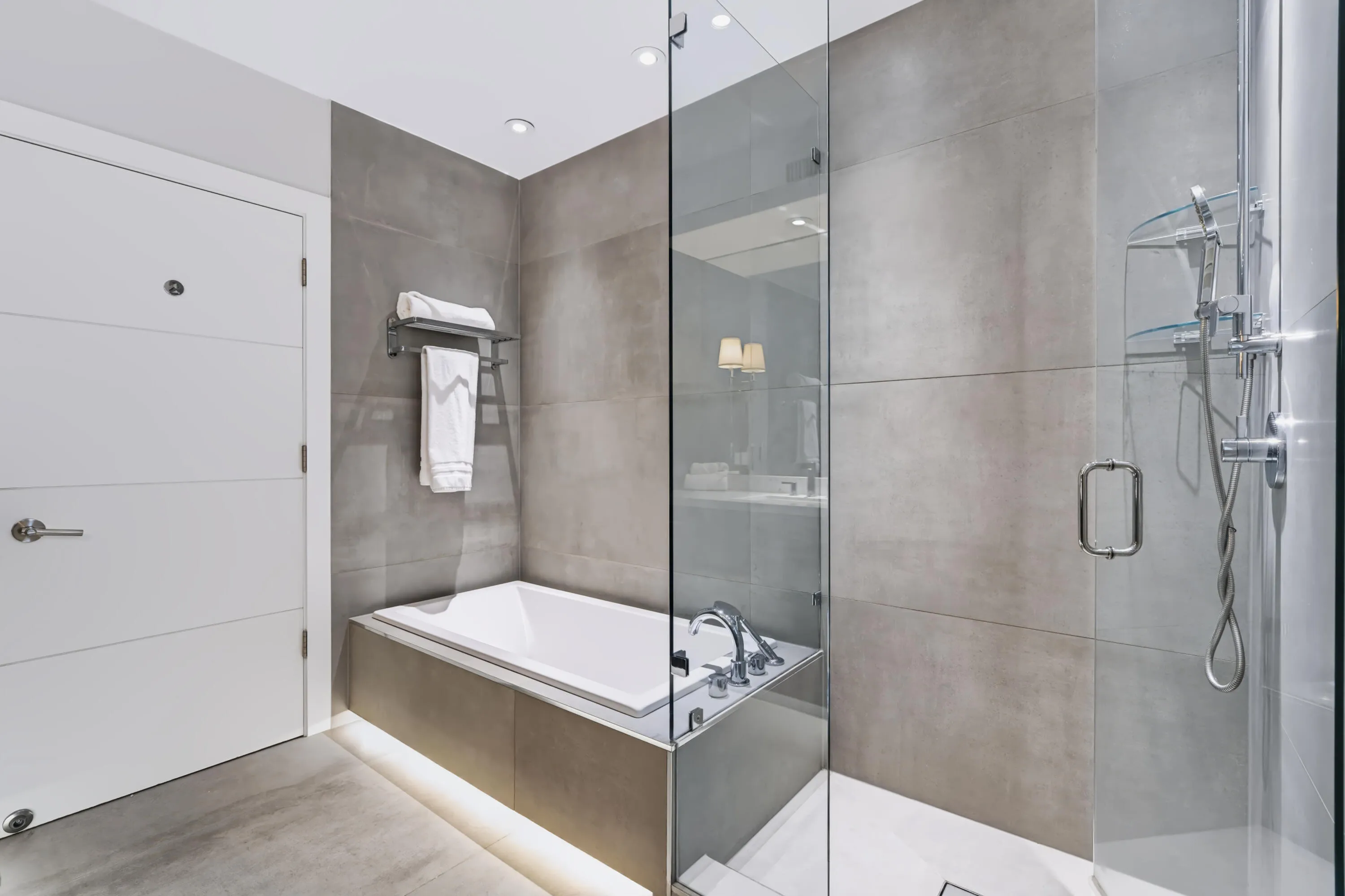 Walk-in glass shower, recessed bathtub, integrated shower shelving, modern wall tiling, and flush-mounted ceiling lighting