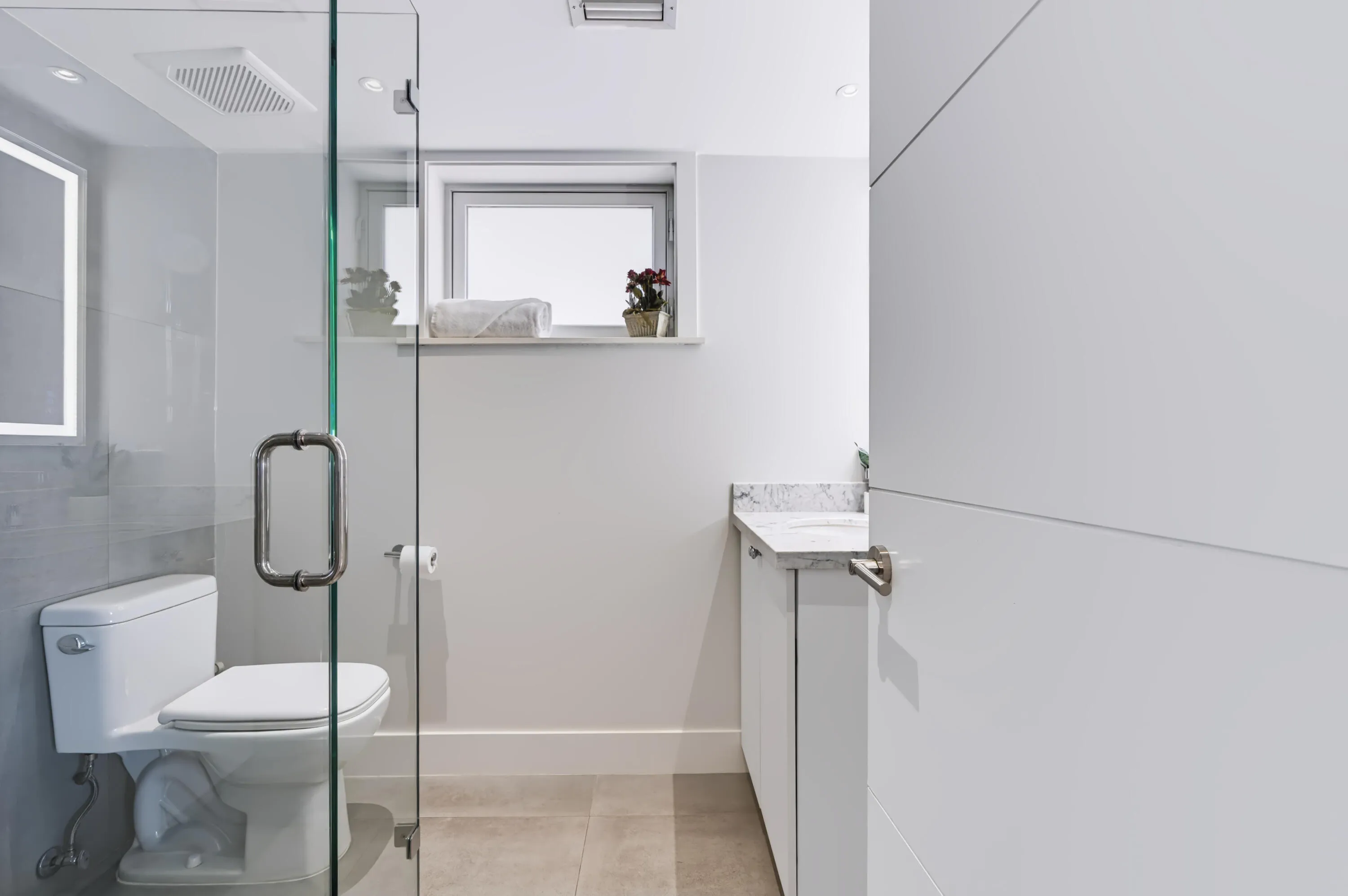 White vanity with a stone countertop, modern white toilet, and a glass shower enclosure with a metal handle