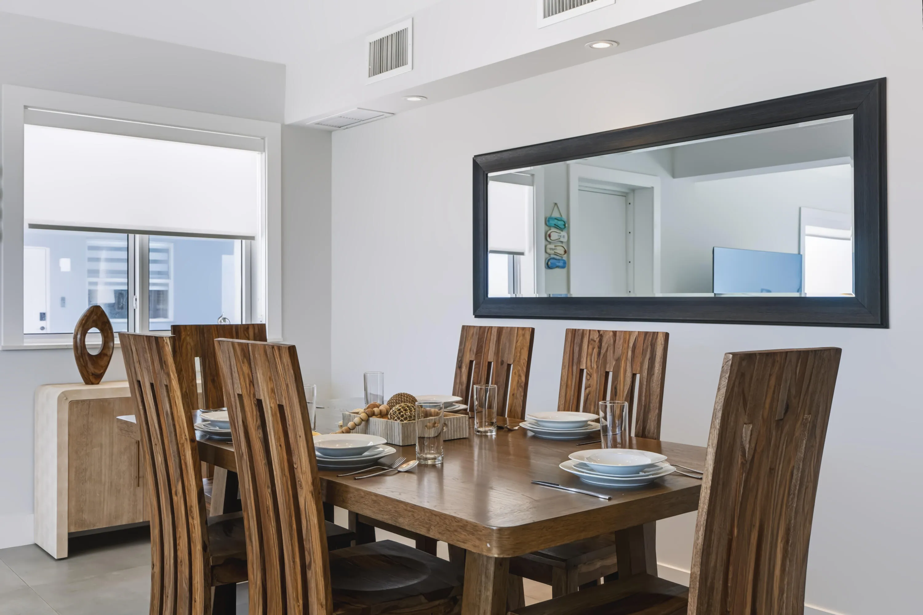 Dining area with a window, wood-finish table, wood-finish chairs, and a large wall-mounted mirror