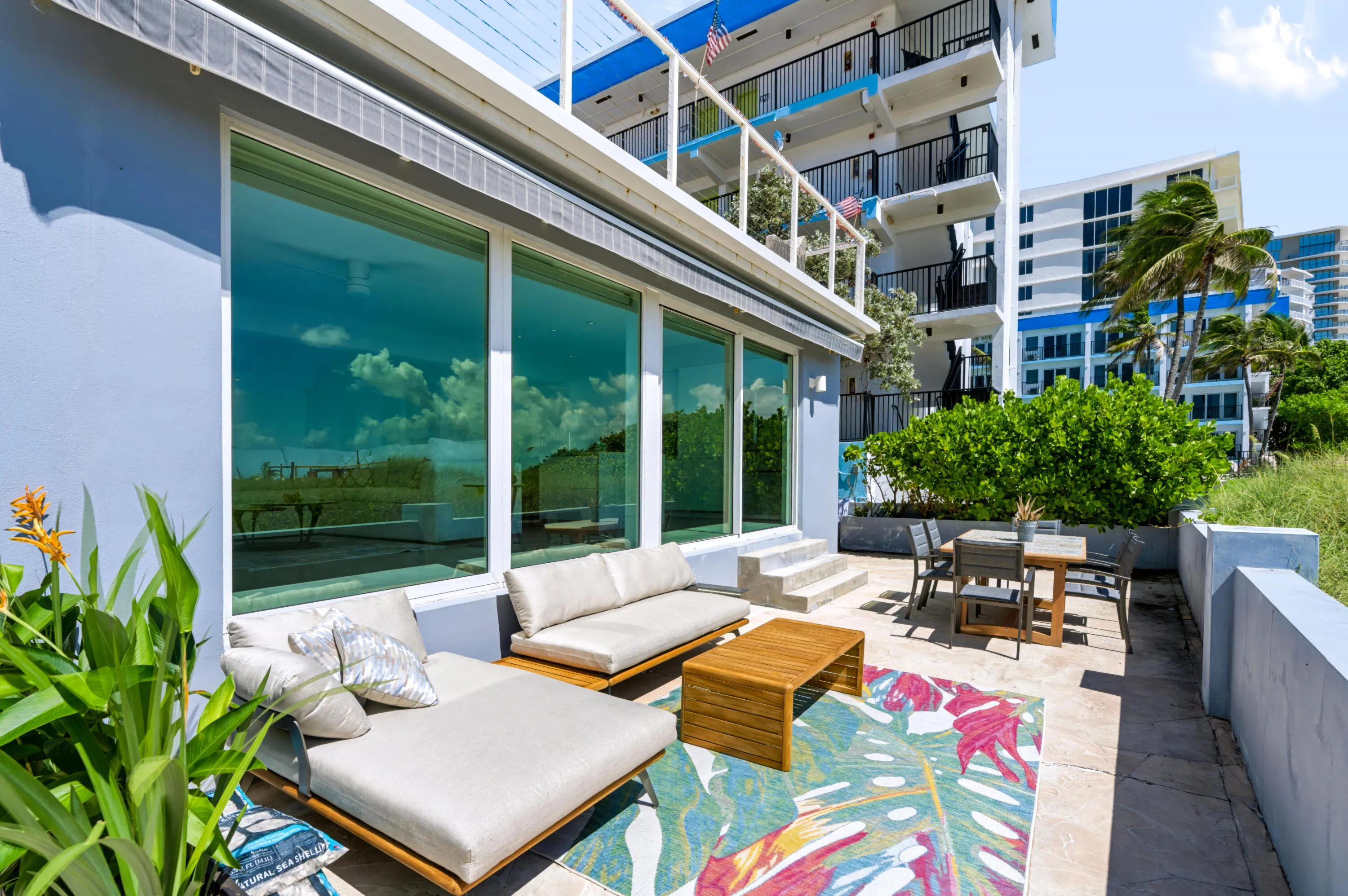 Expansive outdoor patio with stone surfacing, large sliding glass panels, retractable awning, and integrated landscaping