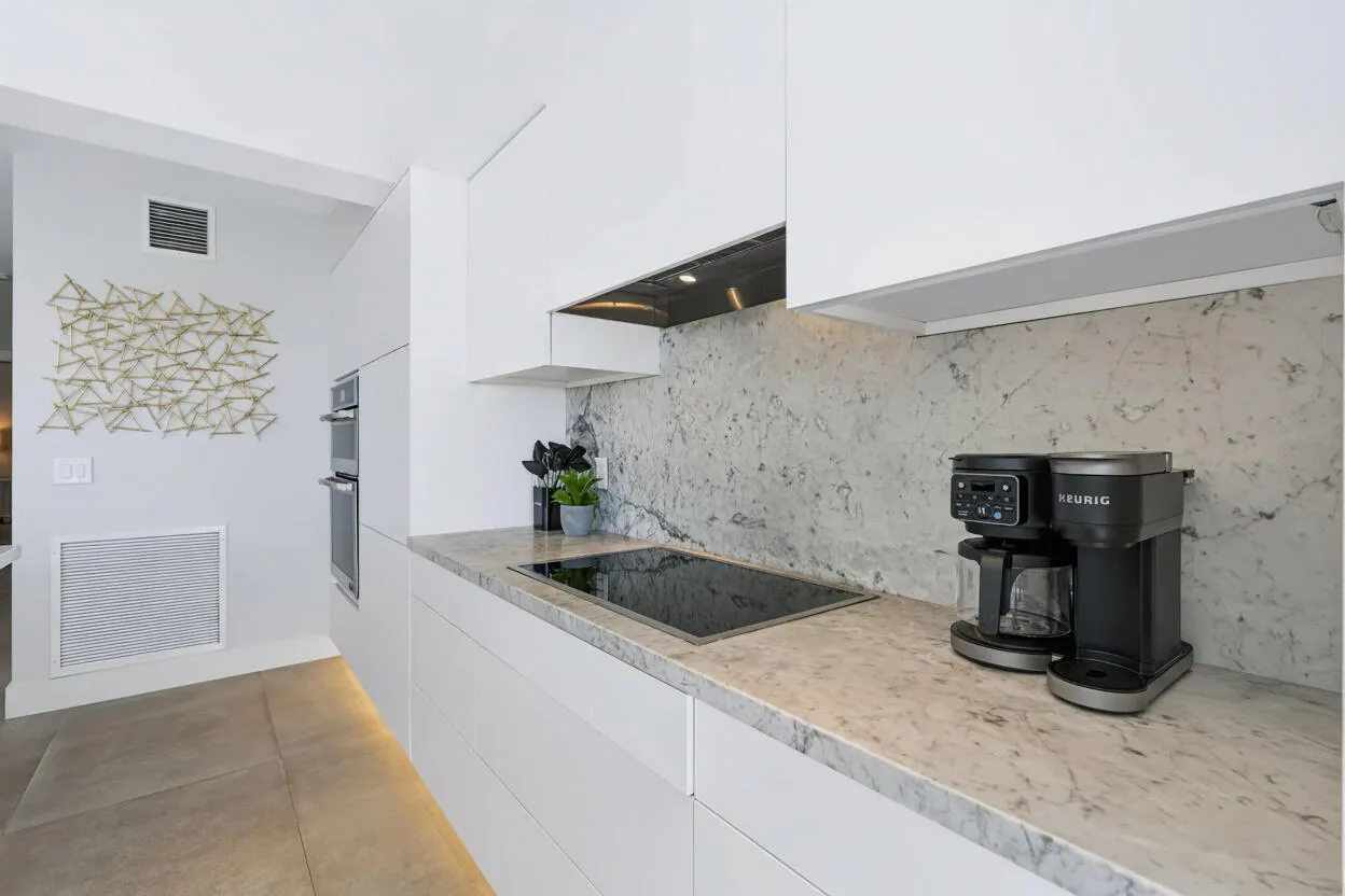 Modern kitchen featuring a seamless white cabinet system, integrated induction cooktop, double wall ovens, and a natural stone countertop with matching backsplash