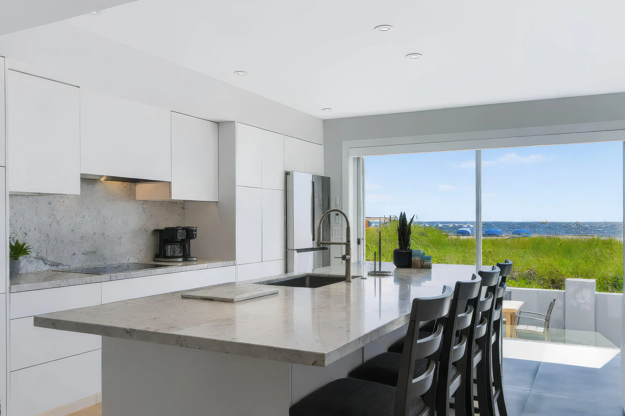 Kitchen featuring white flat-panel cabinetry, a light-toned stone countertop, a stainless steel sink with a gooseneck faucet, and an integrated refrigerator