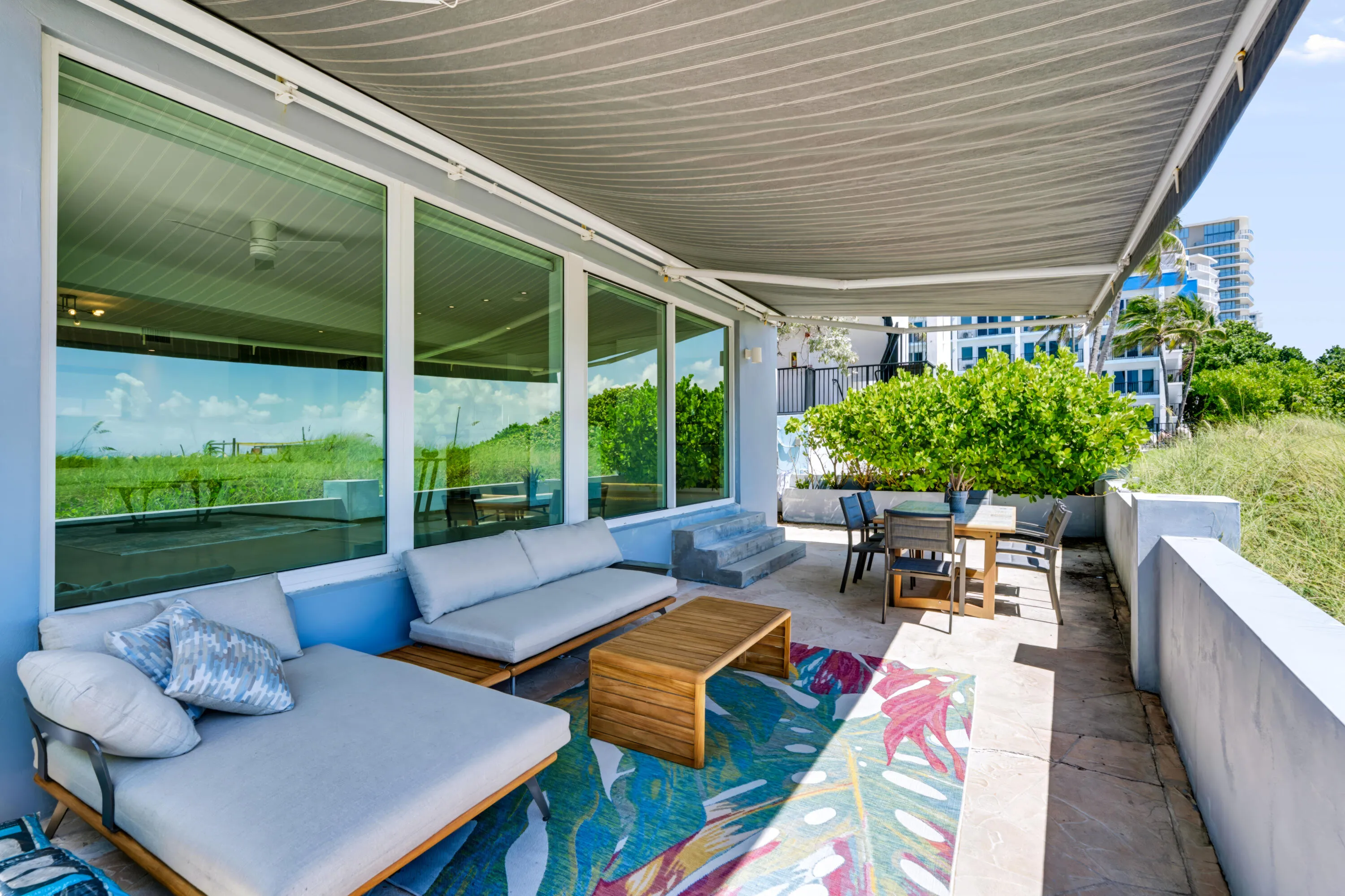 Expansive private patio featuring a retractable awning, large format windows, a low privacy wall, and a raised planter with mature greenery