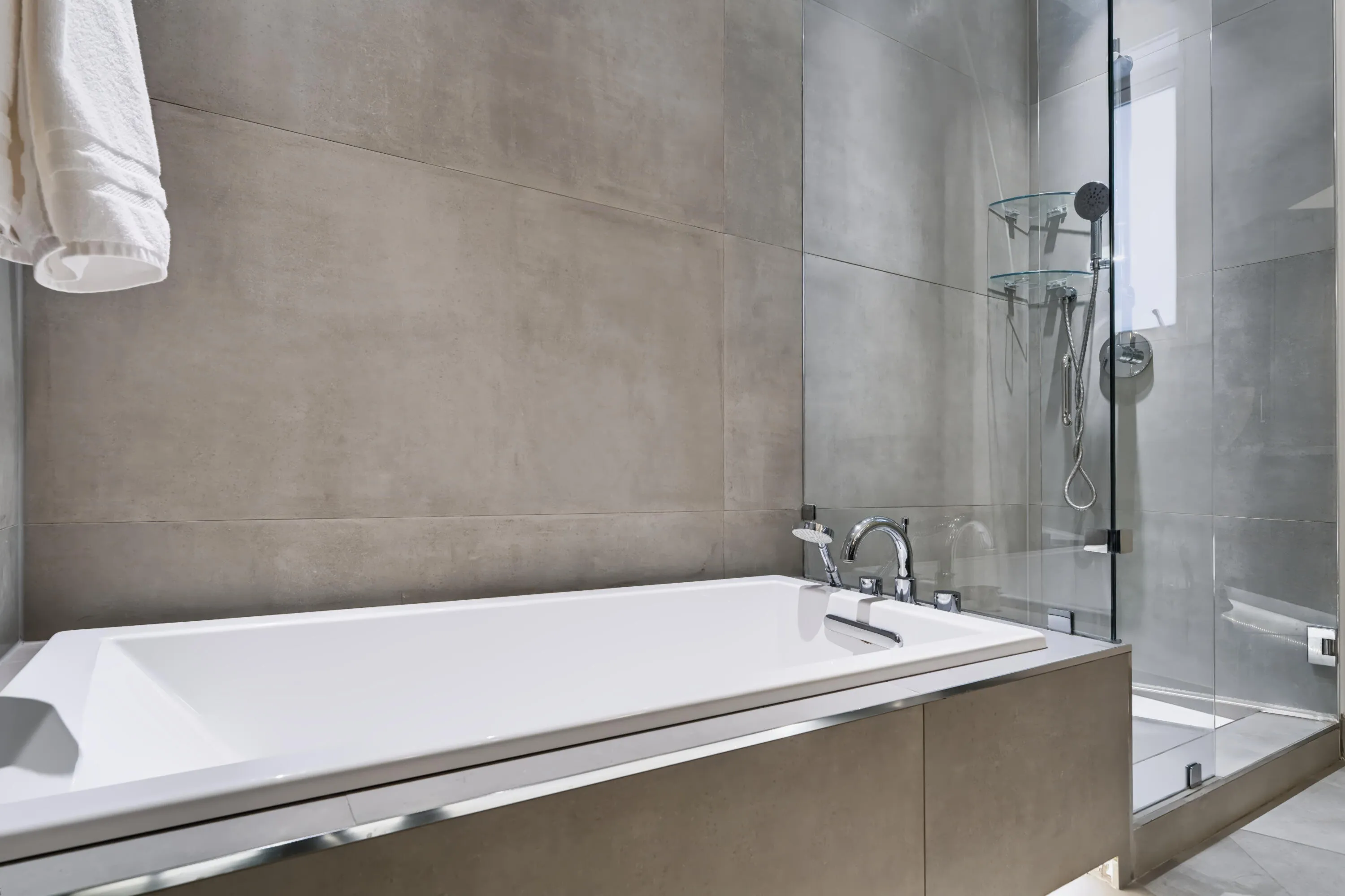 Freestanding bathtub with polished chrome fixtures, glass-enclosed shower, and large format wall tiling