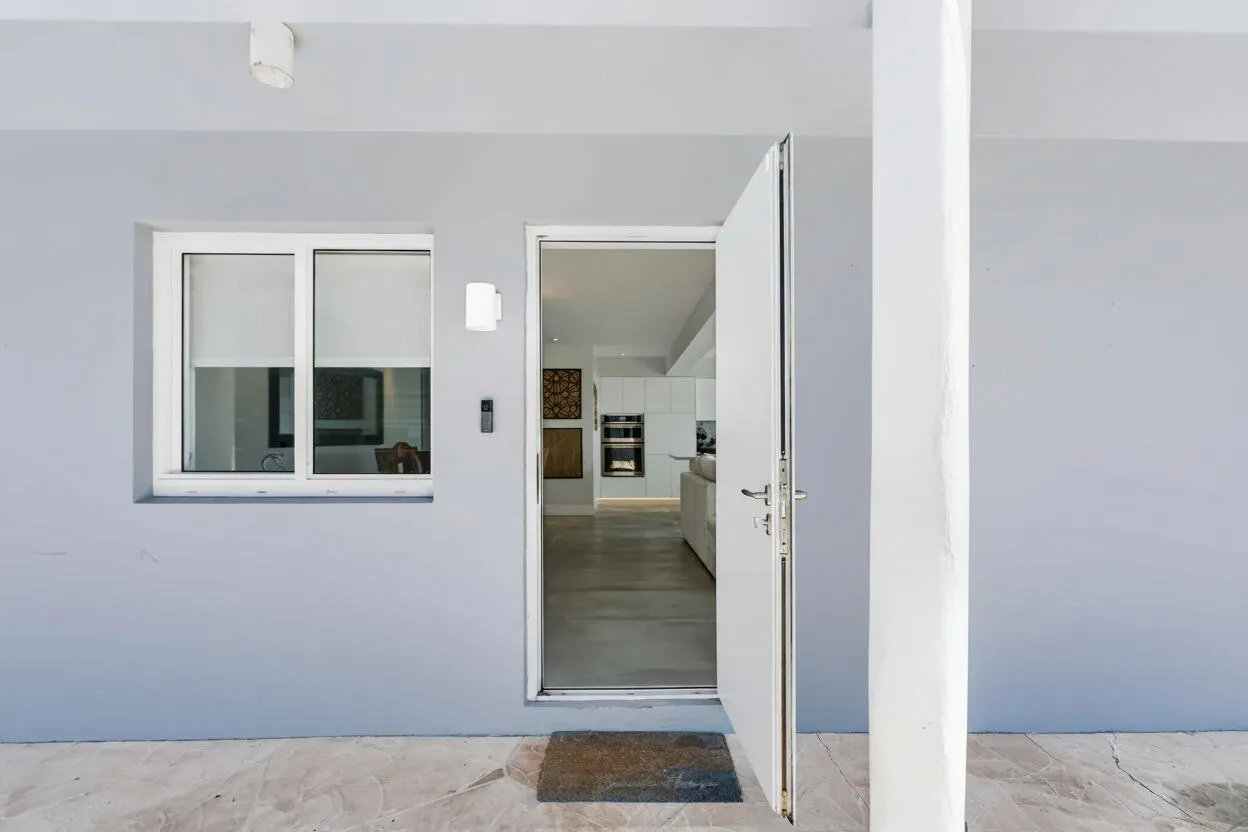 Light gray exterior wall with a white-framed window, an exterior wall sconce, and a white entry door