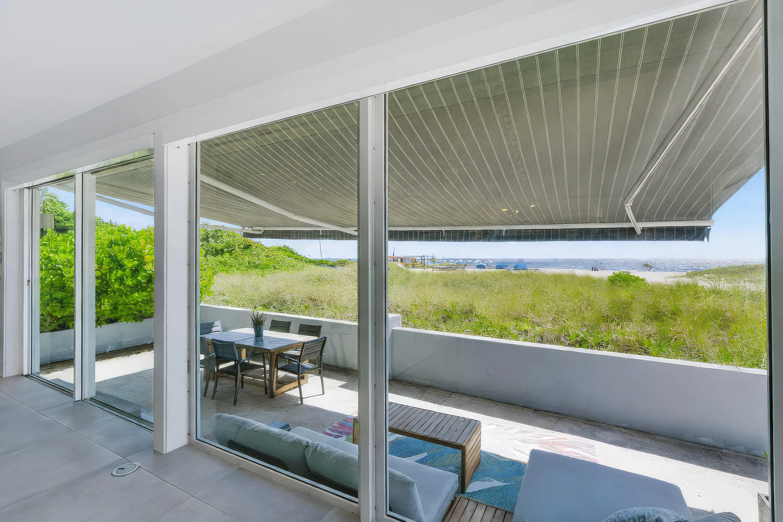 Sliding glass doors opening to an expansive outdoor patio, featuring a striped retractable awning and a white retaining wall