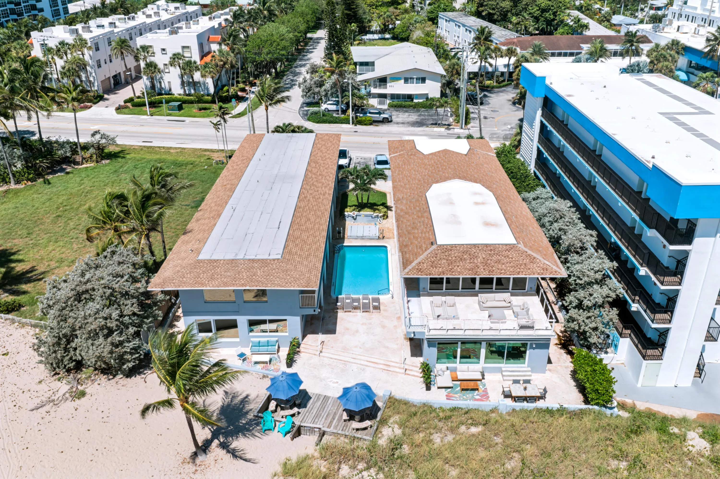 Two distinct structures with shingle roofs, a central swimming pool, and a wooden deck leading to a sandy area
