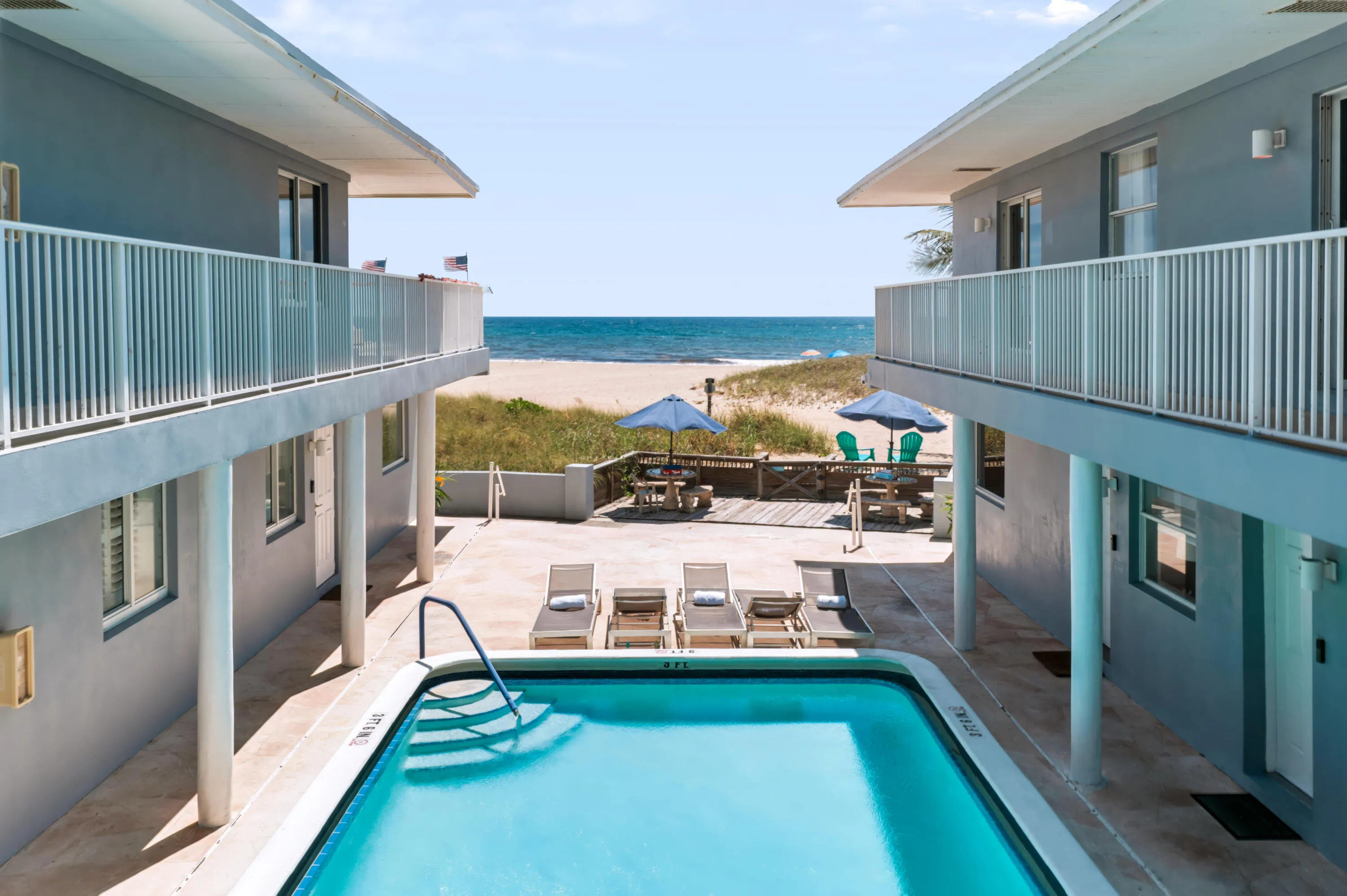 Beachfront property featuring a rectangular swimming pool with integrated steps, concrete pool deck, and upper-level balconies with white railings