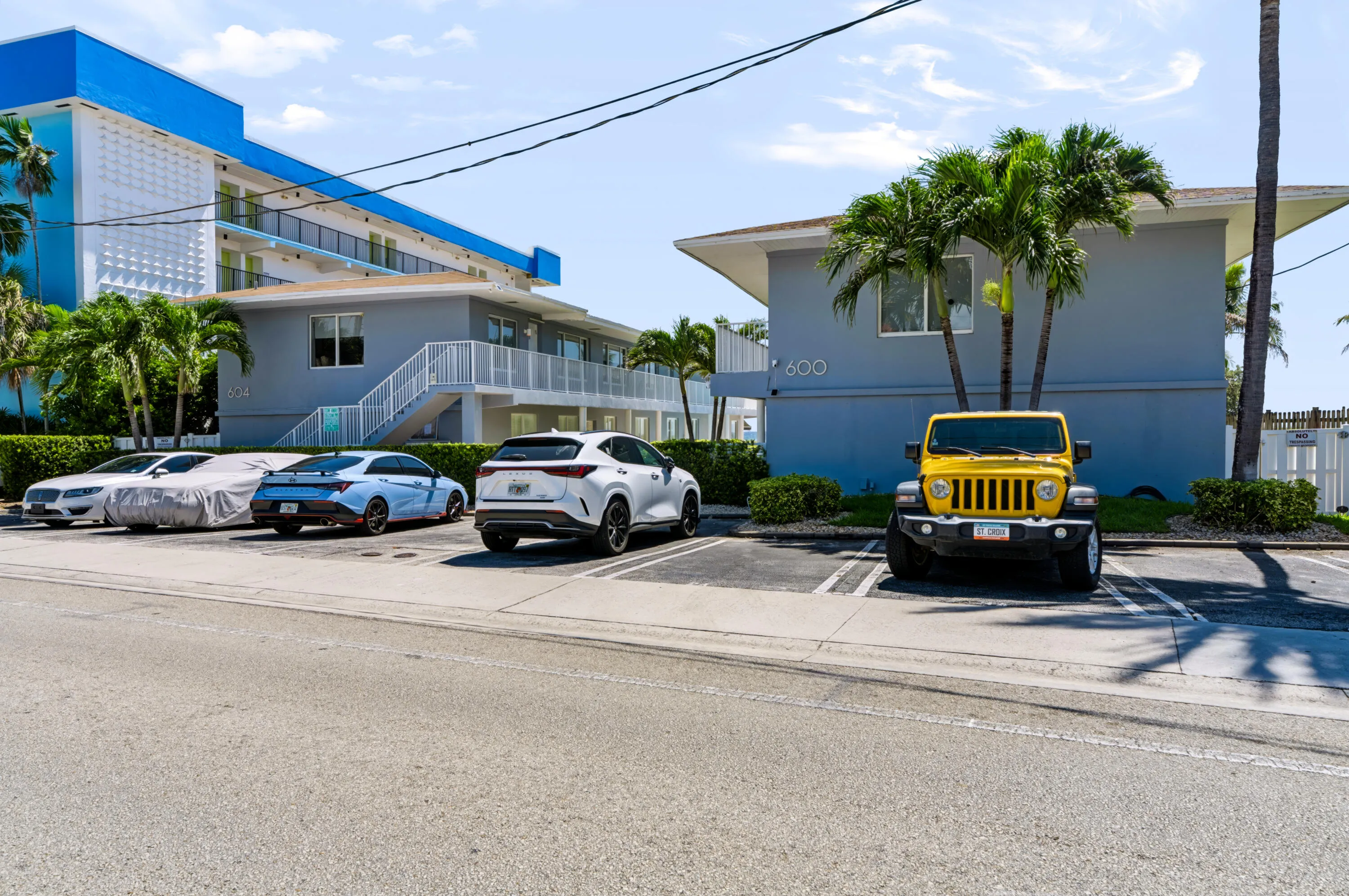 Multi-story buildings with balconies, mature palm trees, and dedicated surface parking