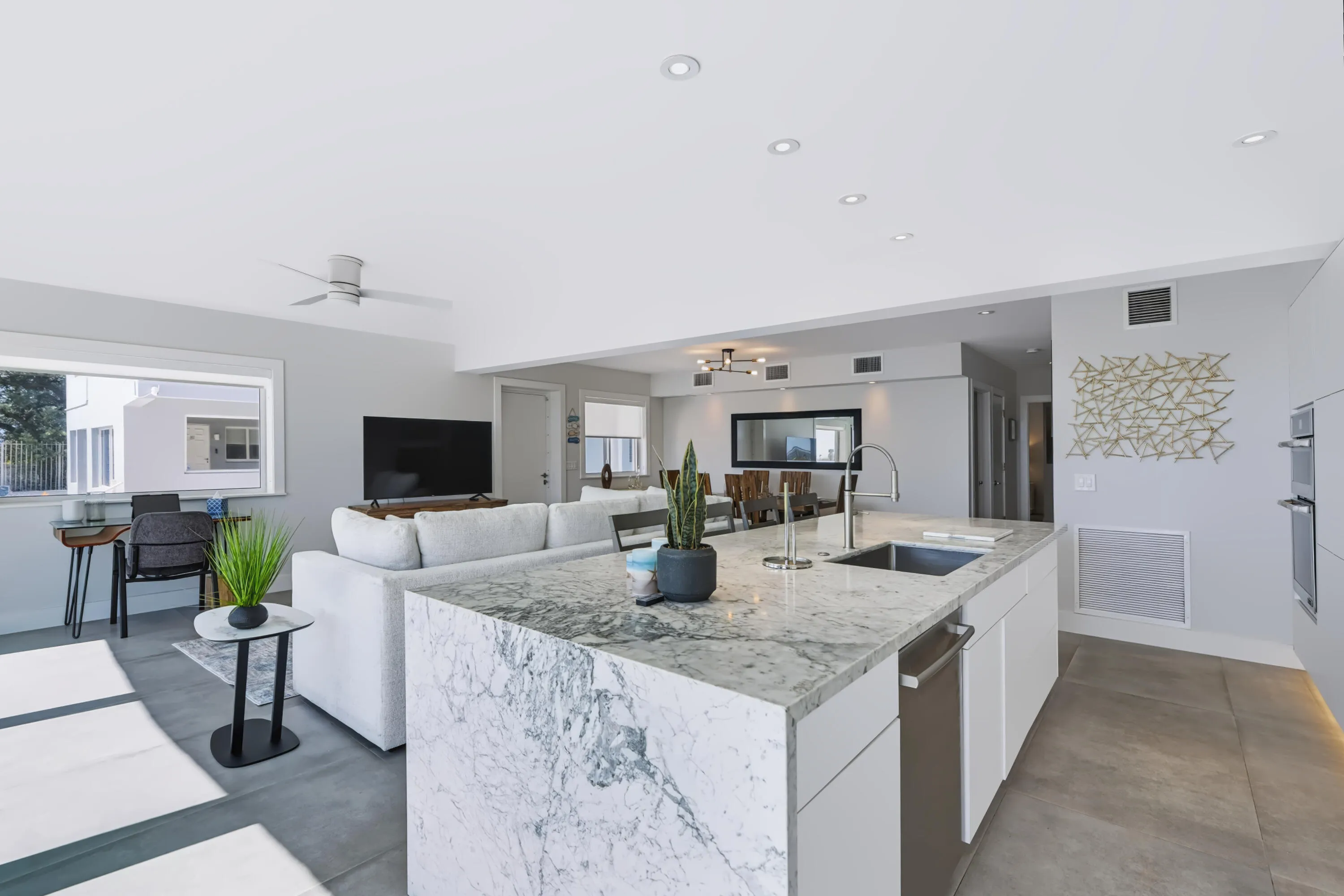 Open-concept living area featuring a kitchen island with stone countertops, recessed lighting, a modern ceiling fan, and built-in wall ovens