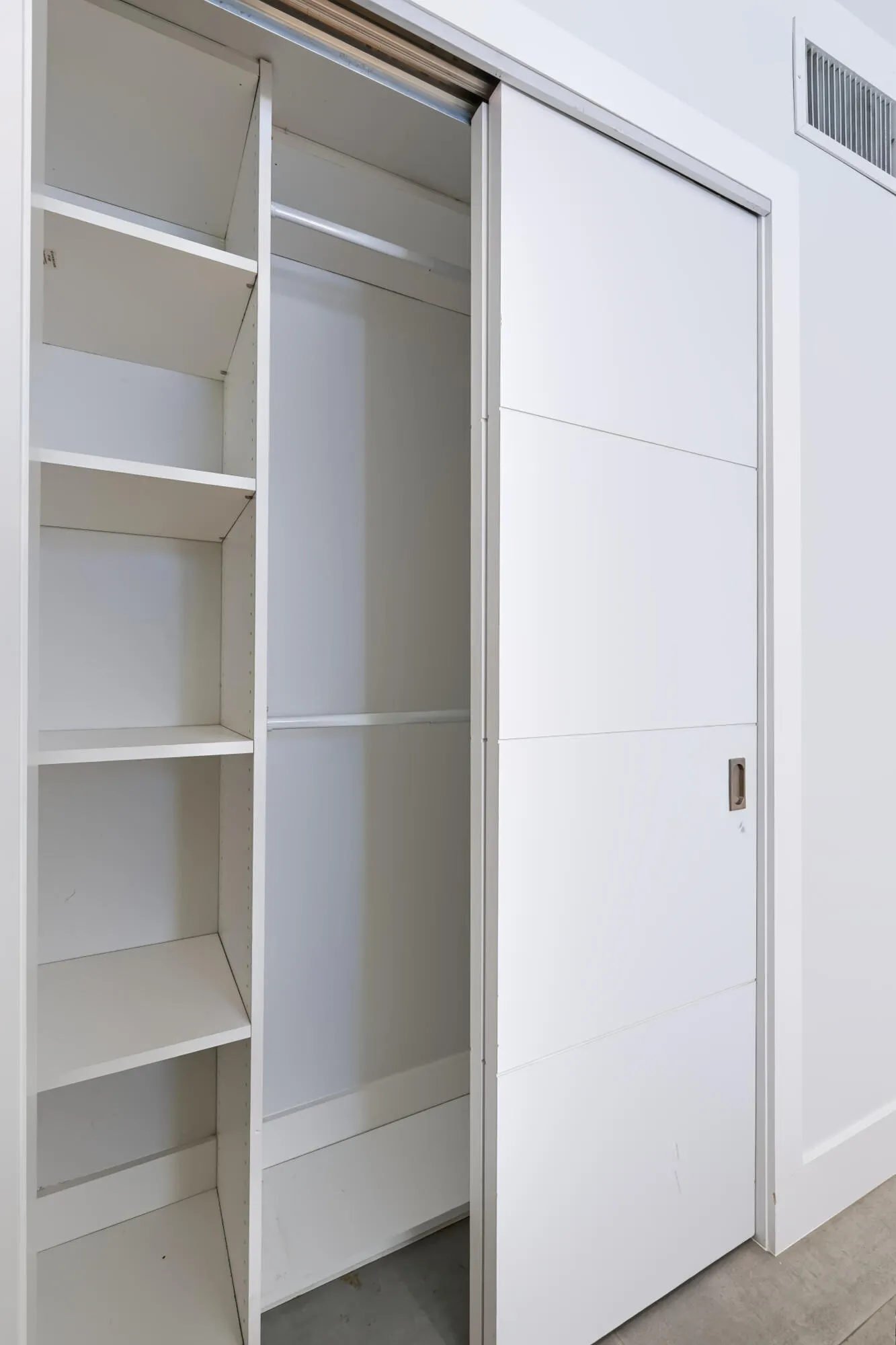 Built-in closet system with multiple shelving units and clothing rods, featuring a white sliding door with horizontal paneling