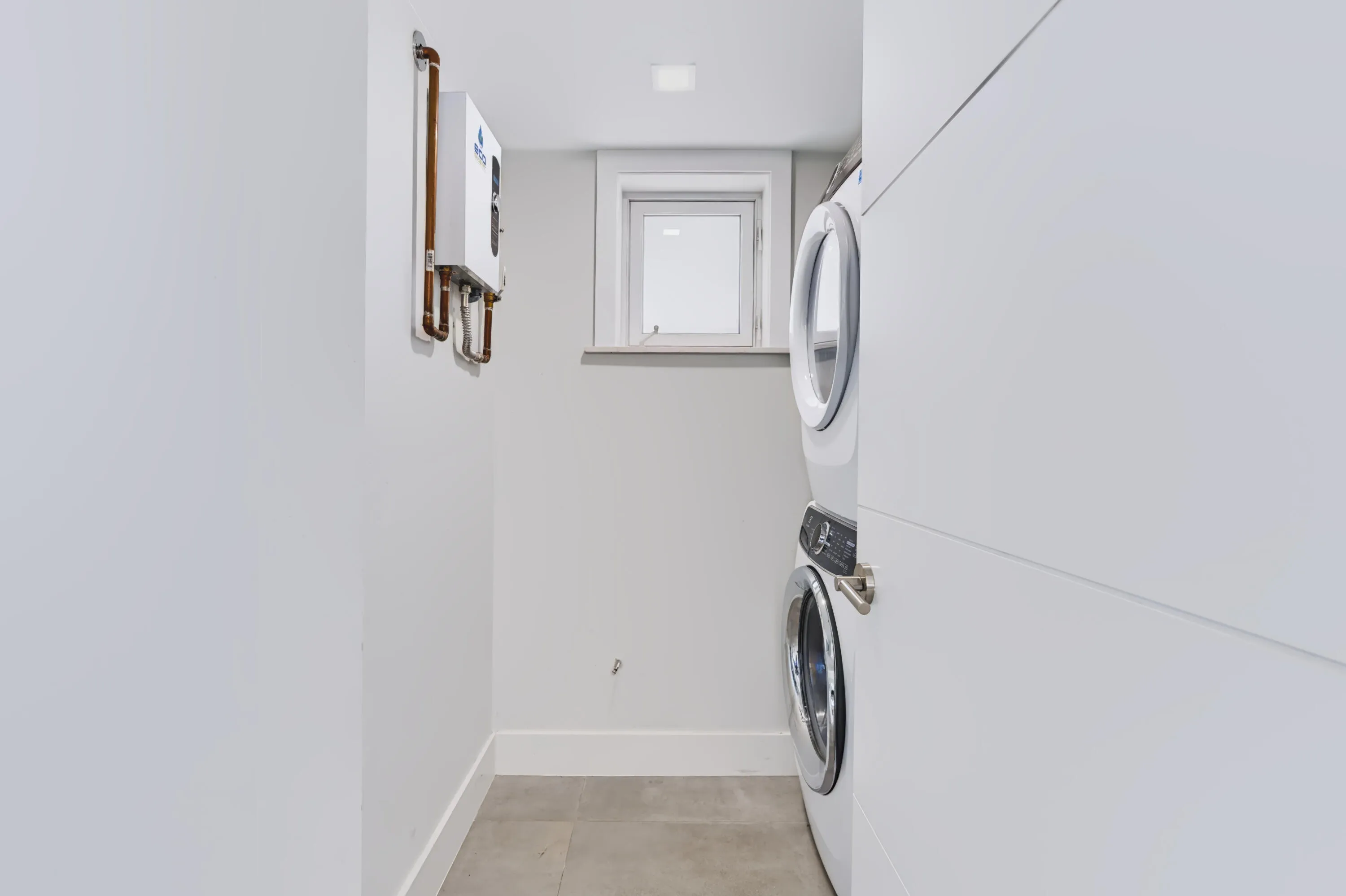 Stackable washer and dryer, square window, light gray floor tiling, and a wall-mounted water heater