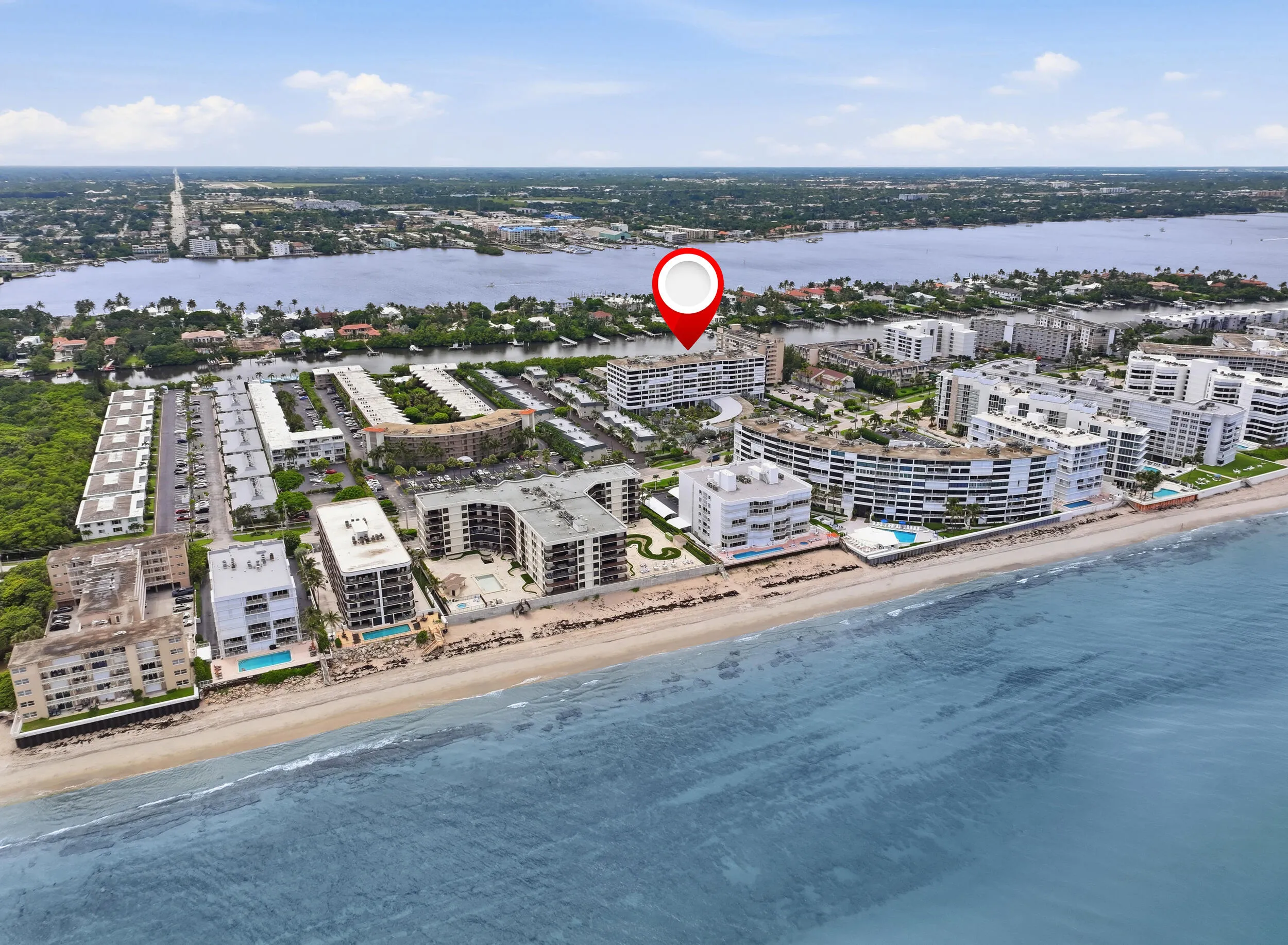 Coastal multi-story building situated on a sandy beachfront with surrounding residential structures and waterfront access