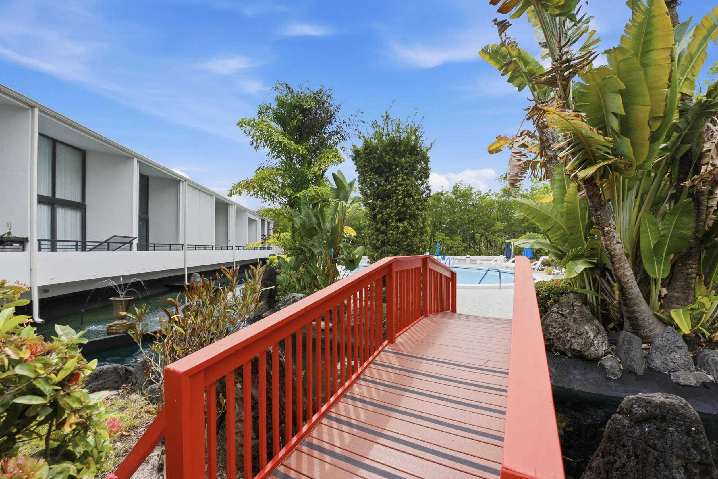 Vibrant red pedestrian bridge over a water feature, bordered by lush tropical landscaping