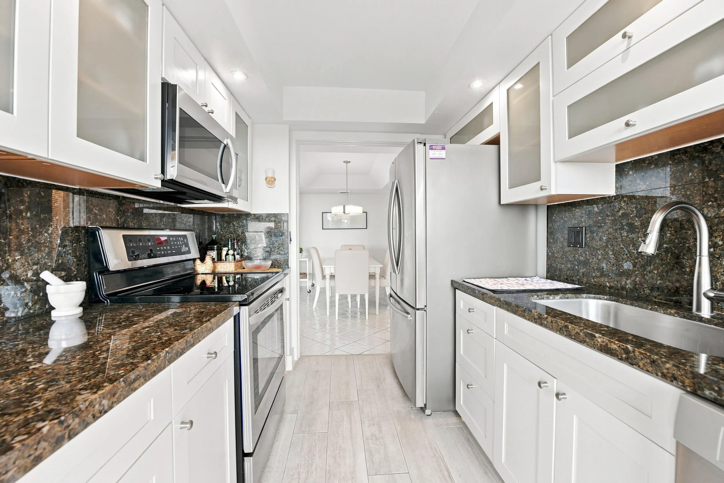 Galley kitchen featuring white cabinetry with frosted glass inserts, dark speckled countertops, and a matching full-height backsplash