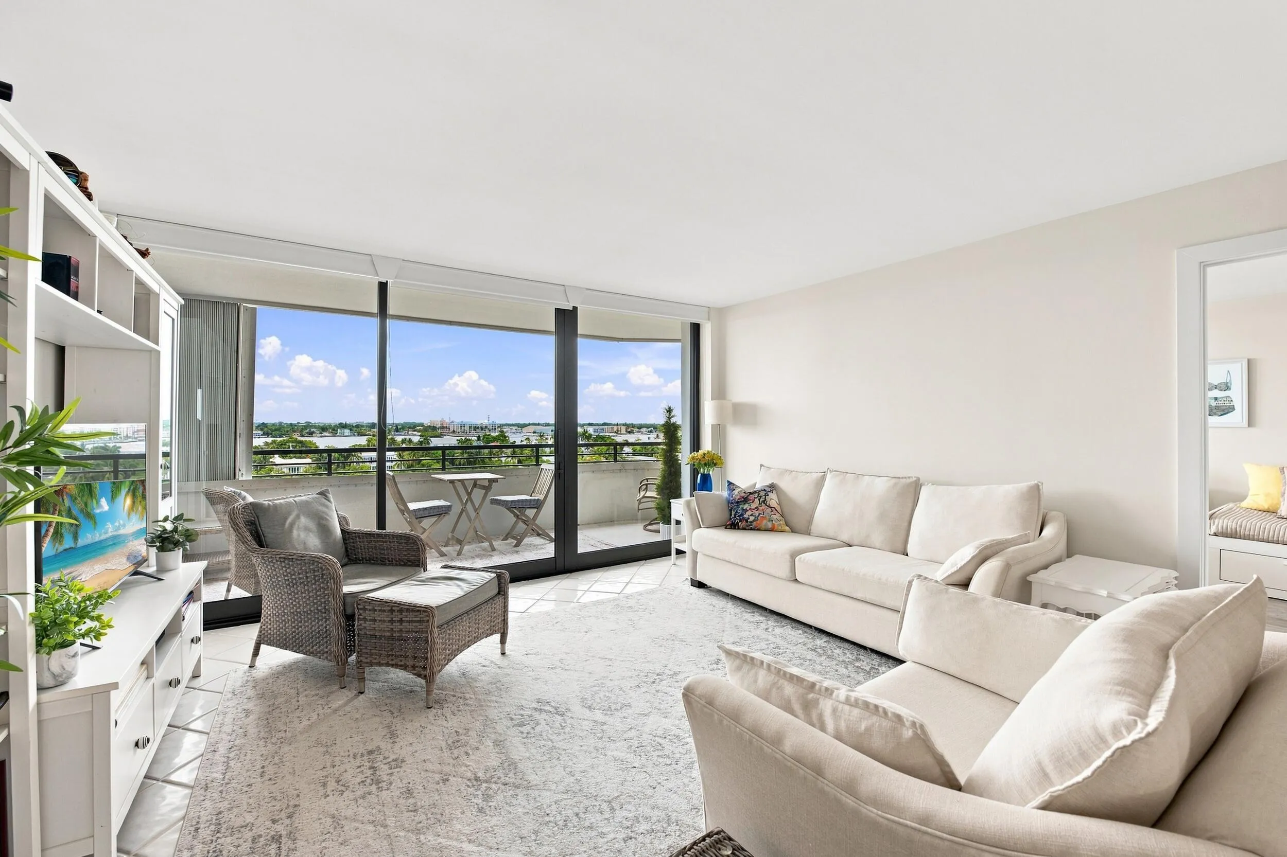 Spacious living area featuring floor-to-ceiling windows, a private balcony with water and city views, and light-toned tile flooring
